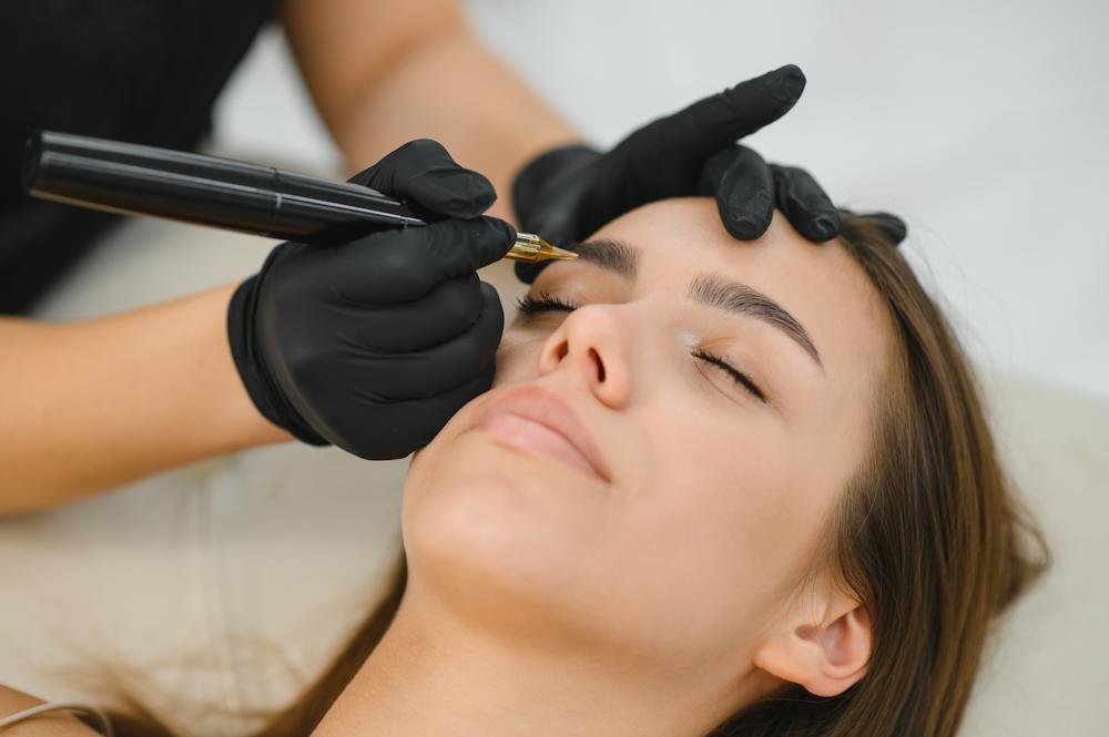 A woman receiving an eyebrow tattoo or microblading procedure from a professional wearing black gloves.