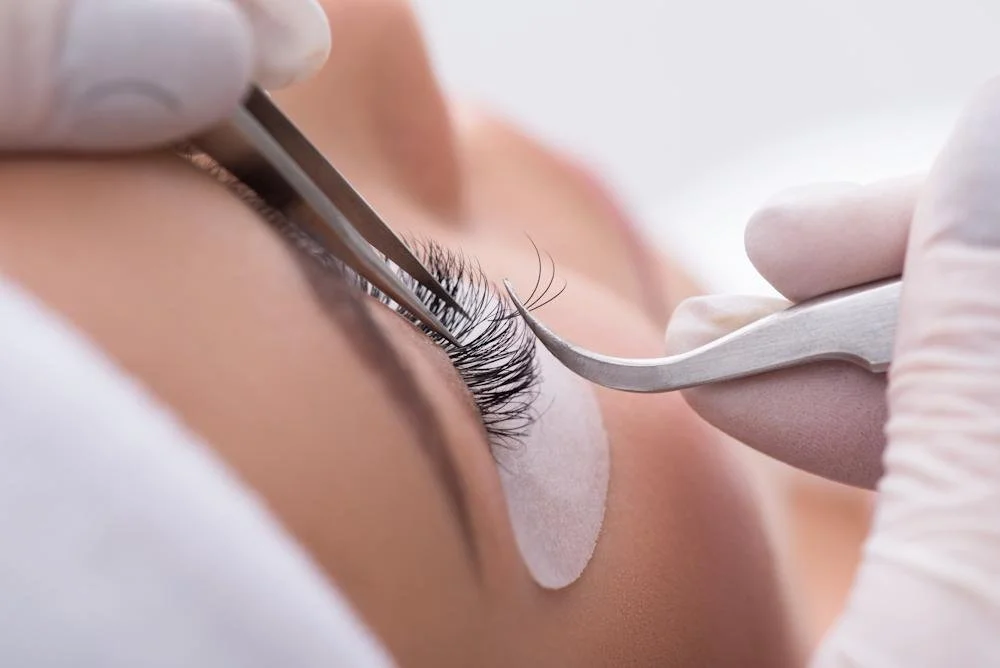 Close-up of an eyelash extension procedure with a technician applying artificial eyelashes near a person's eye.
