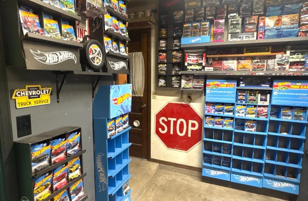A room filled with Hot Wheels toy cars on shelves and display racks, including a large stop sign on the wall.