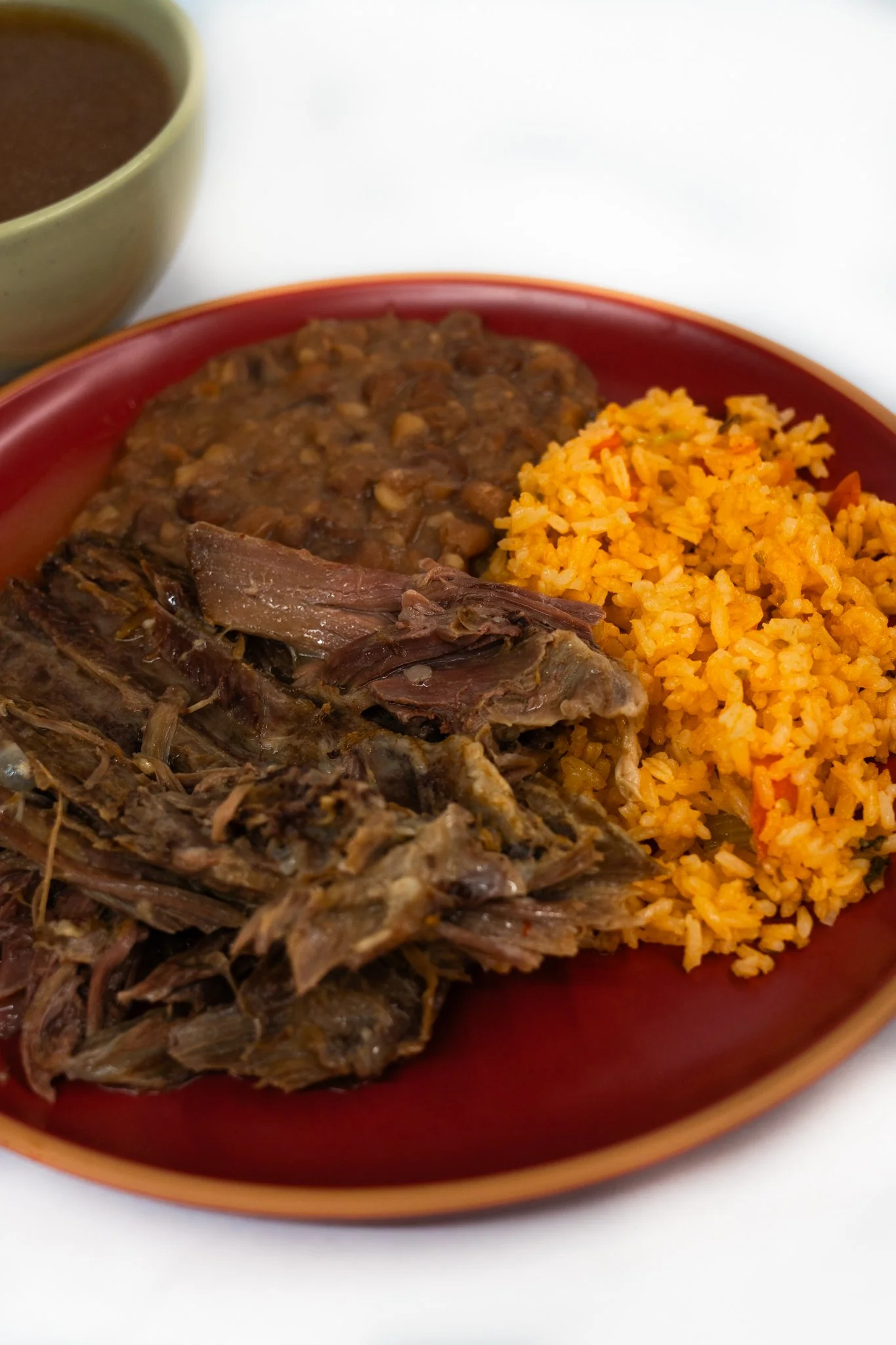 Plate of Mexican tallow, orange rice, and refried beans with a bowl of sauce in the background.