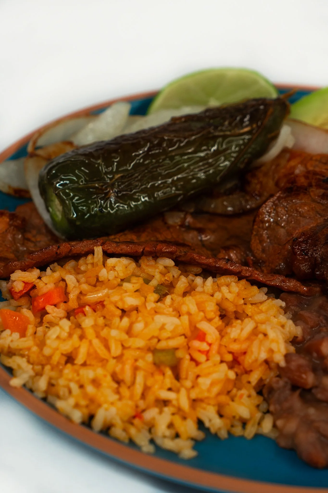 Close-up of Mexican plate with rice, grilled meat, grilled jalapeño pepper, and lime wedge.
