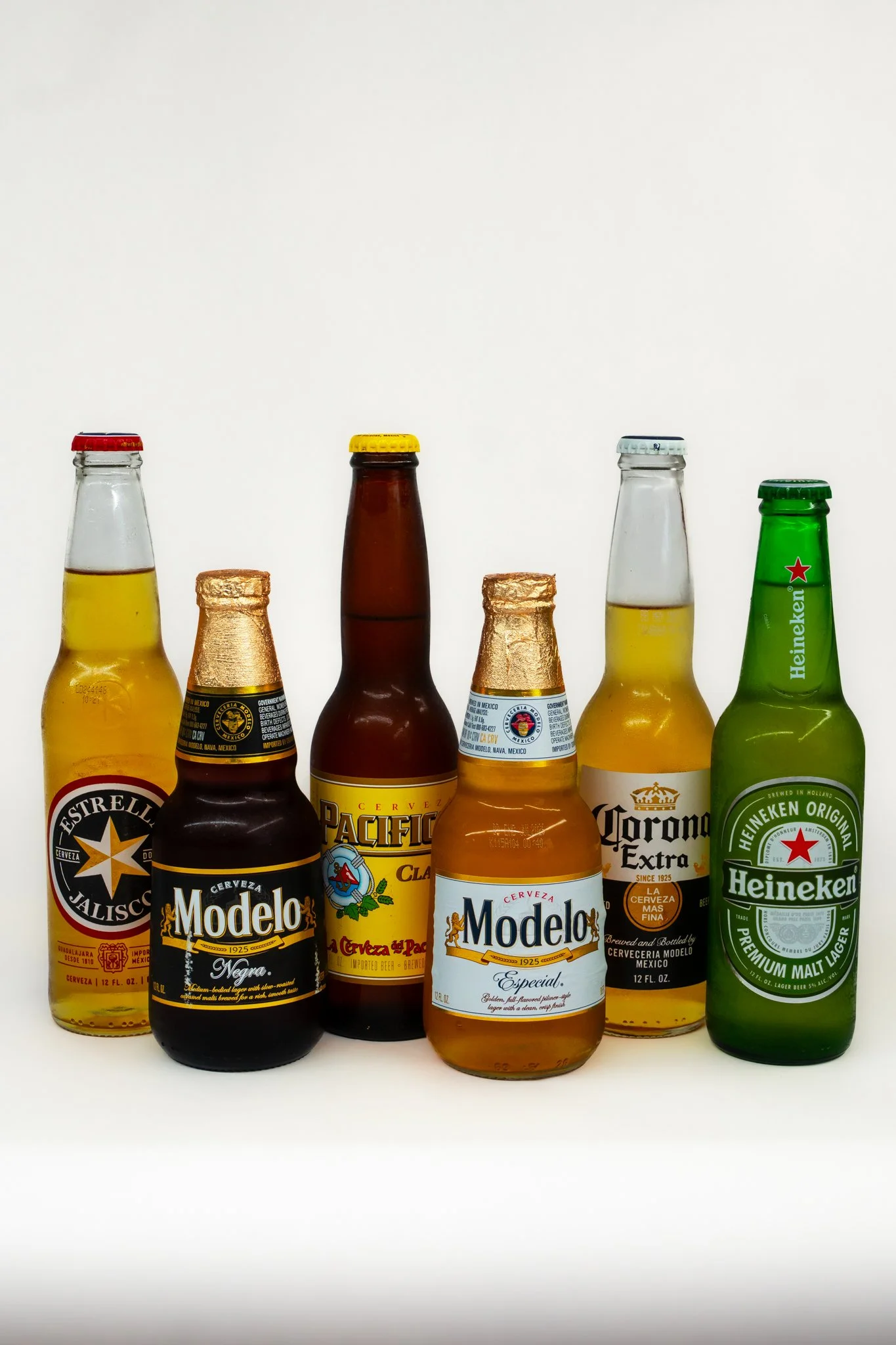 Six beer bottles displayed on a white background, including Estrella Jalisco, Modelo Negra, Pacifico, Modelo Especial, Corona Extra, and Heineken.