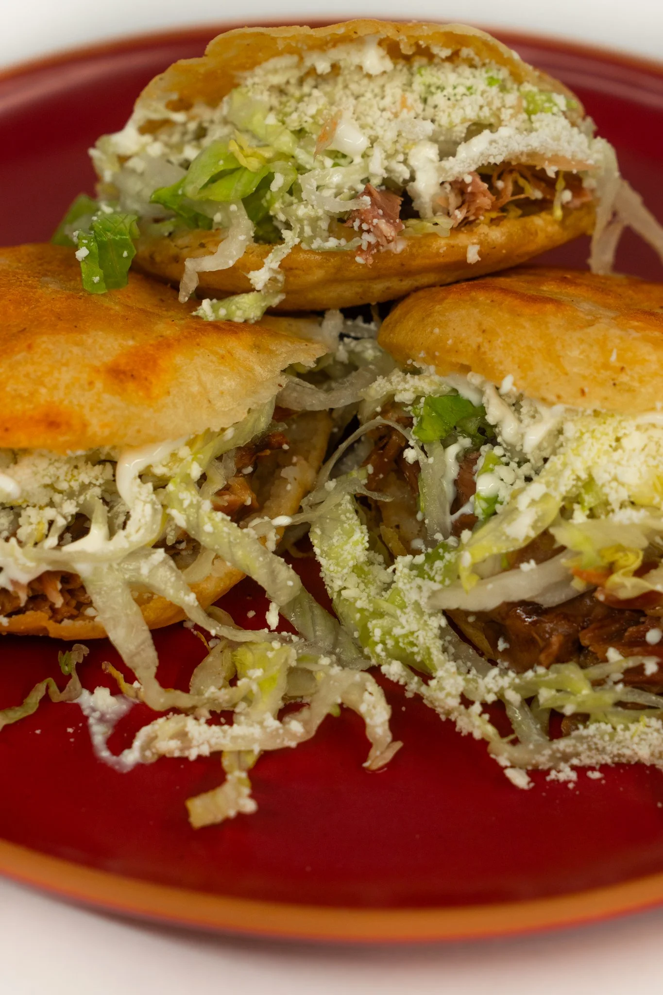 Two Mexican tlayudas filled with lettuce, shredded meat, cheese, and sauce, served on a red plate.