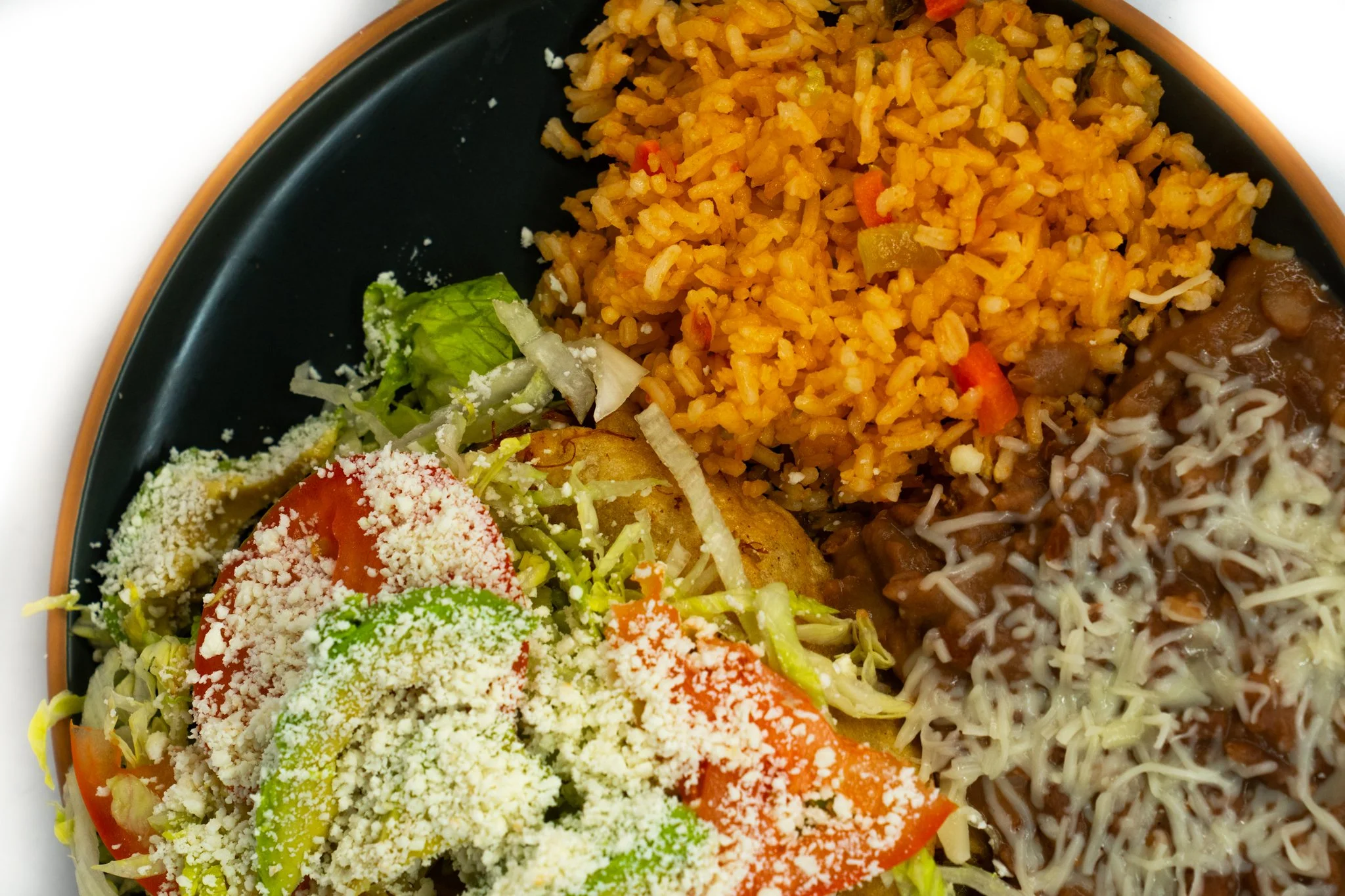A plate of Mexican food with rice, refried beans topped with cheese, and a fresh garden salad with tomatoes, lettuce, and cheese.