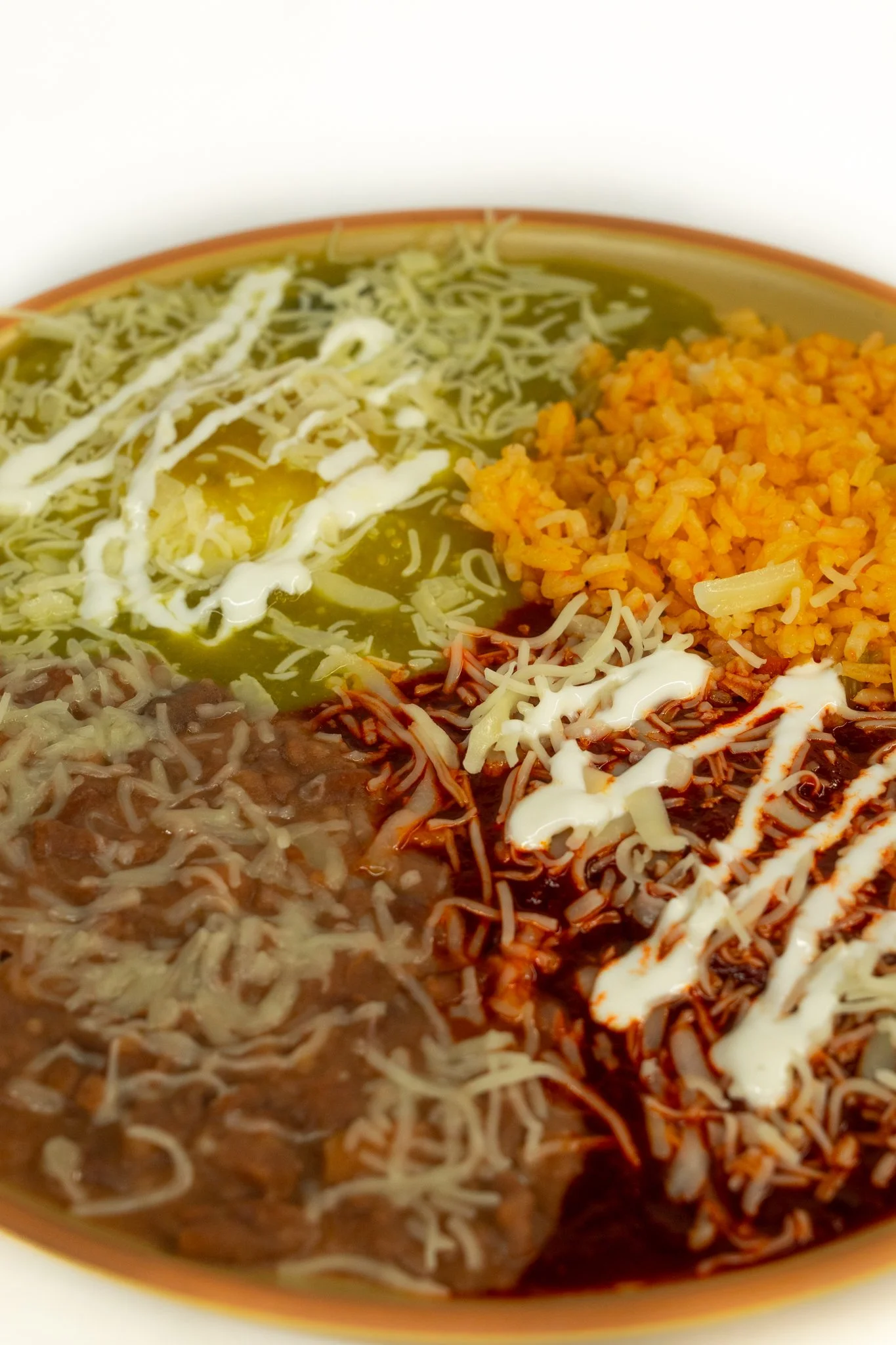 Bowl of Mexican food with rice, shredded cheese, sour cream, beans, and sauce.