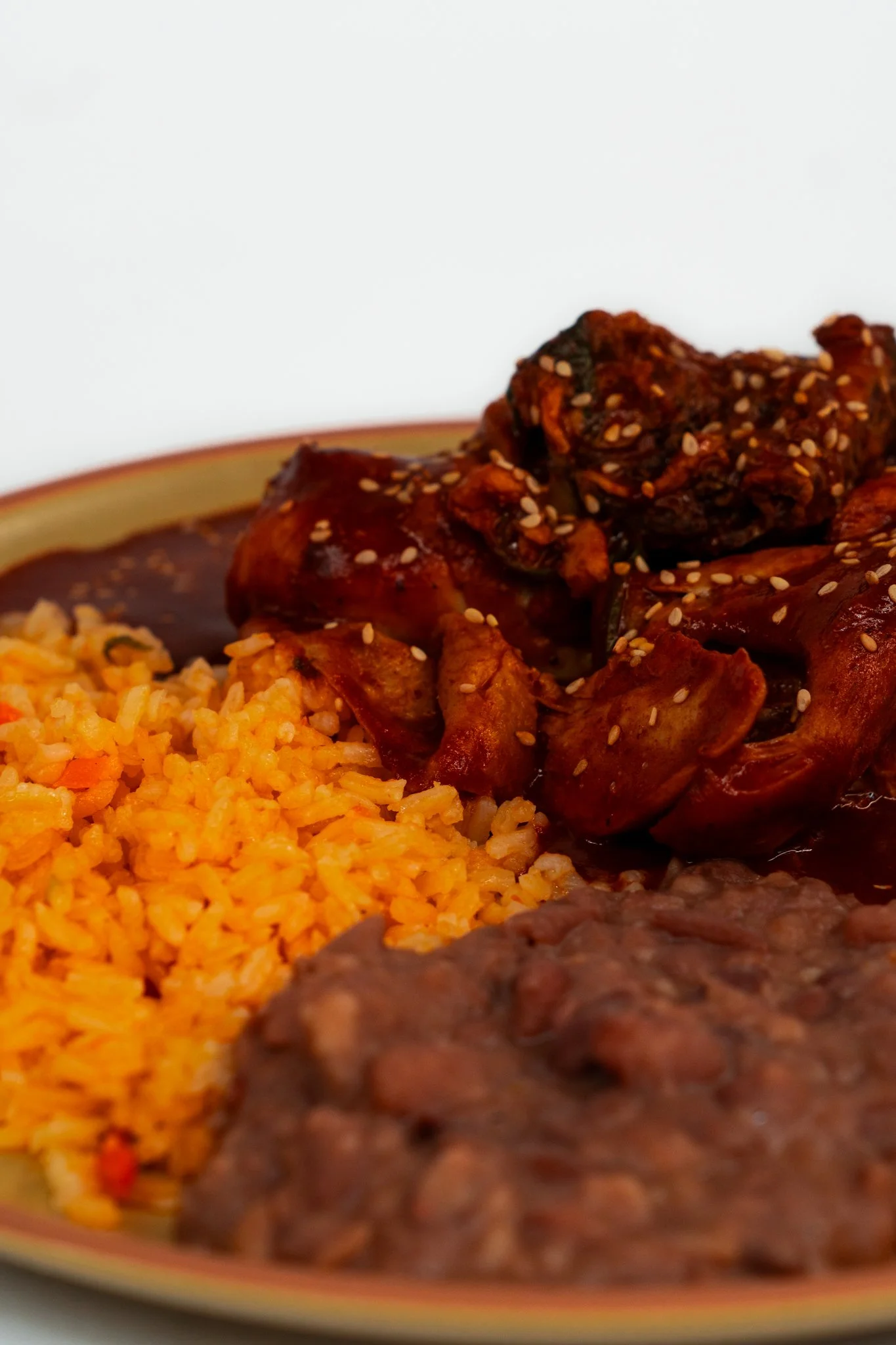 Close-up of a plate with Mexican food, including Mexican rice, refried beans, and beef stew with meat and vegetables, garnished with sesame seeds.