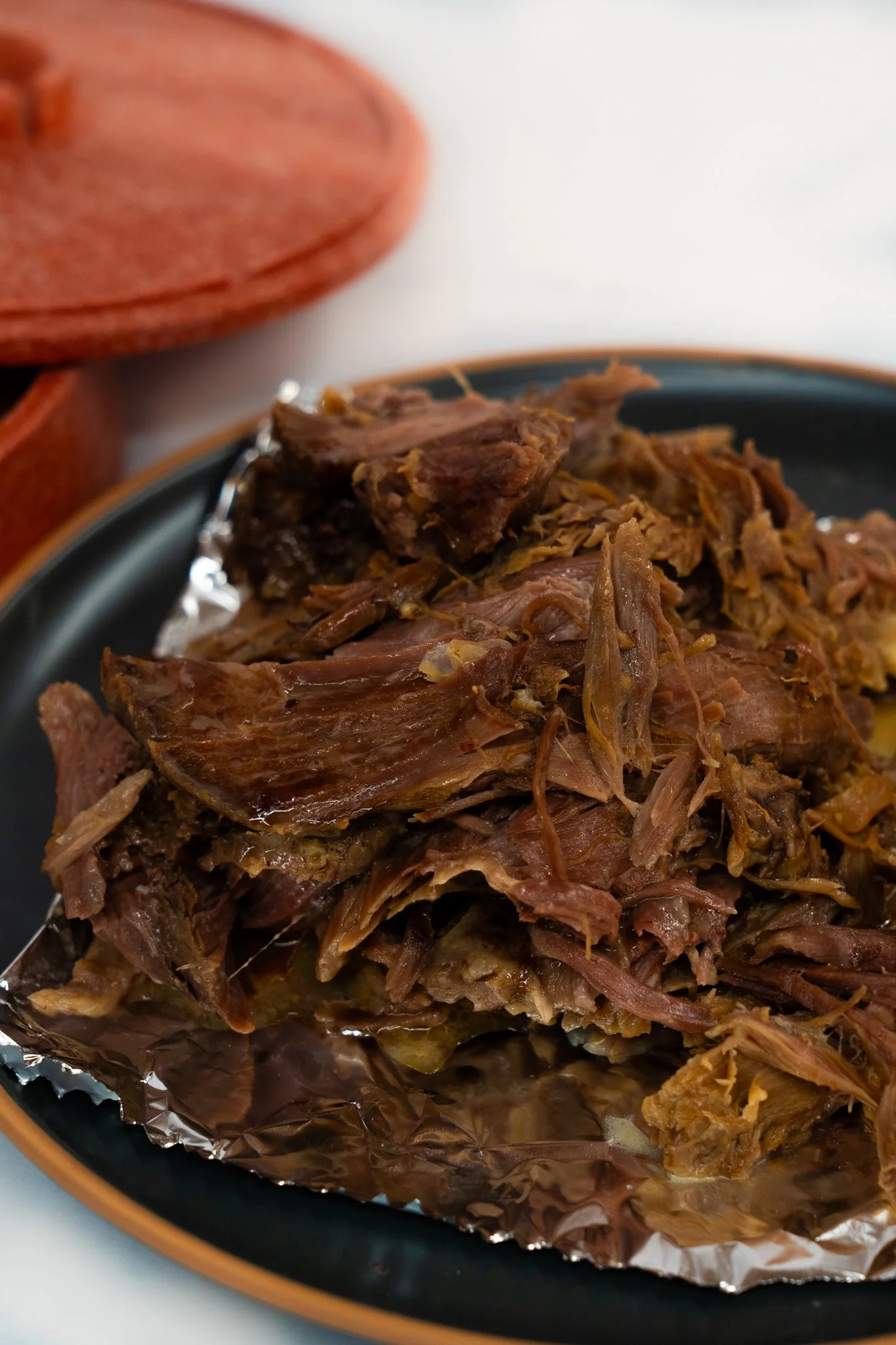 Shredded cooked meat on foil on a black plate in a close-up shot.