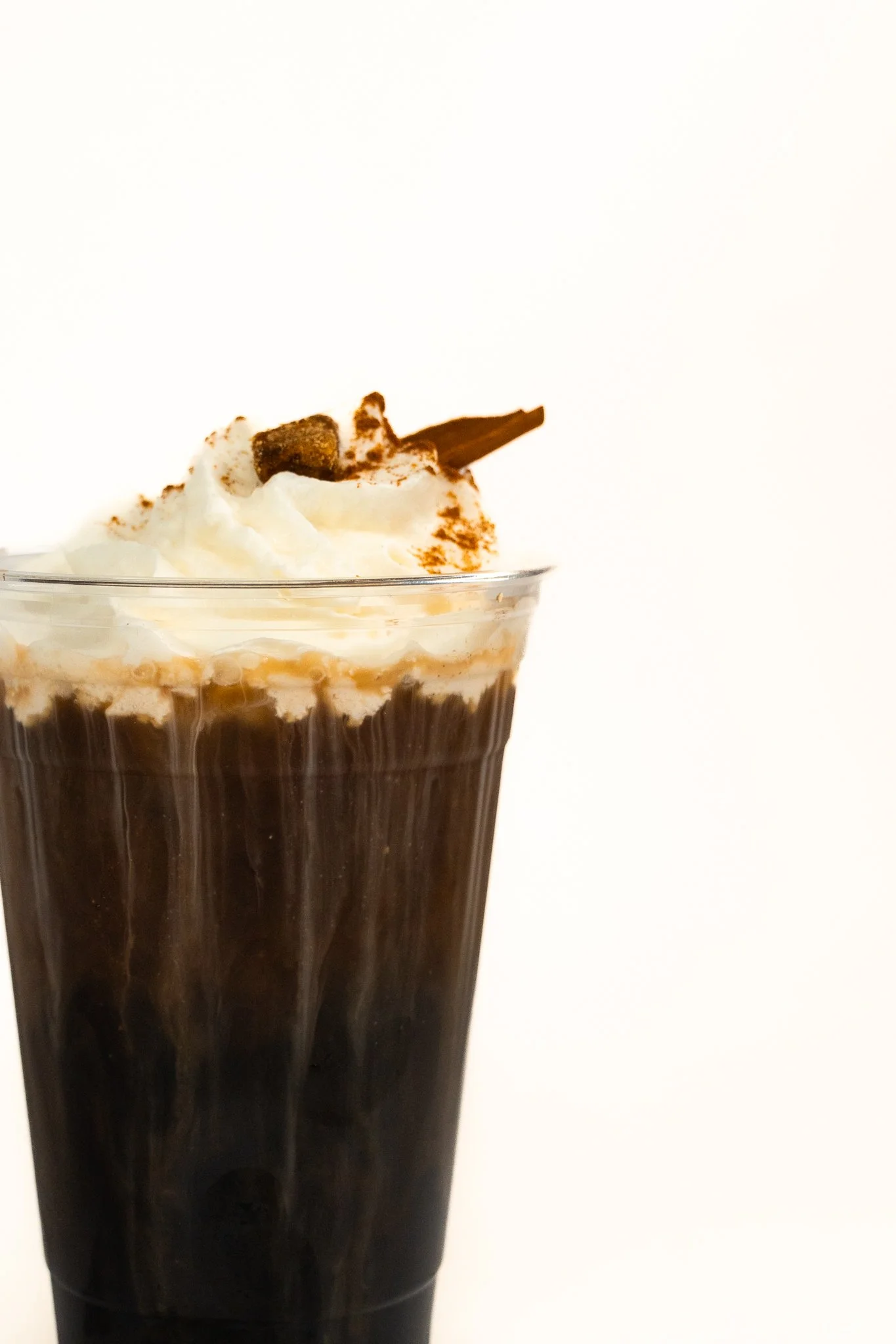 A tall glass of iced coffee topped with whipped cream, chocolate shavings, and a chocolate stick.