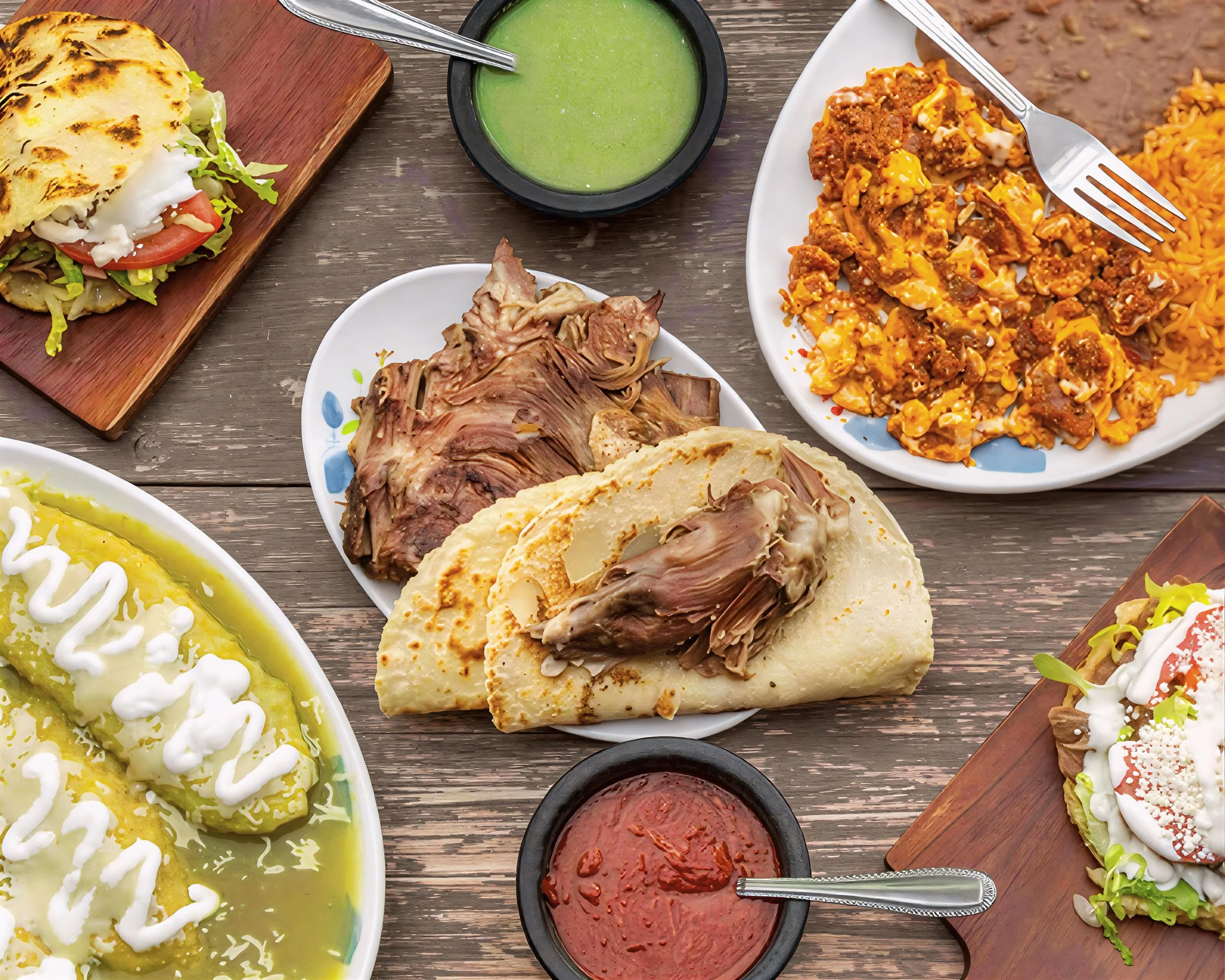 Assorted Mexican dishes on a wooden table, including tacos, rice, and sauce