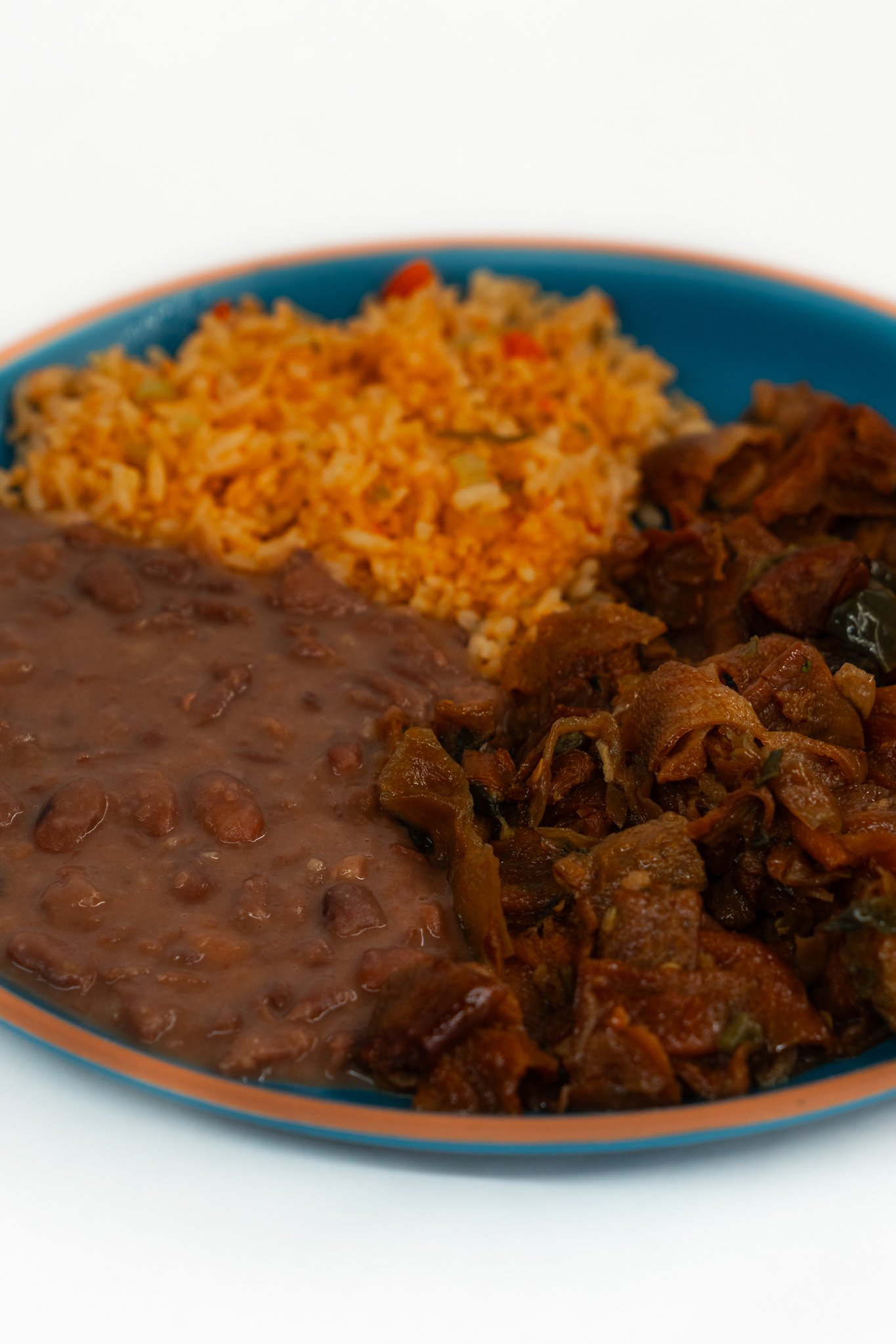 Plate of Mexican food with refried beans, Mexican rice, and beef stew.