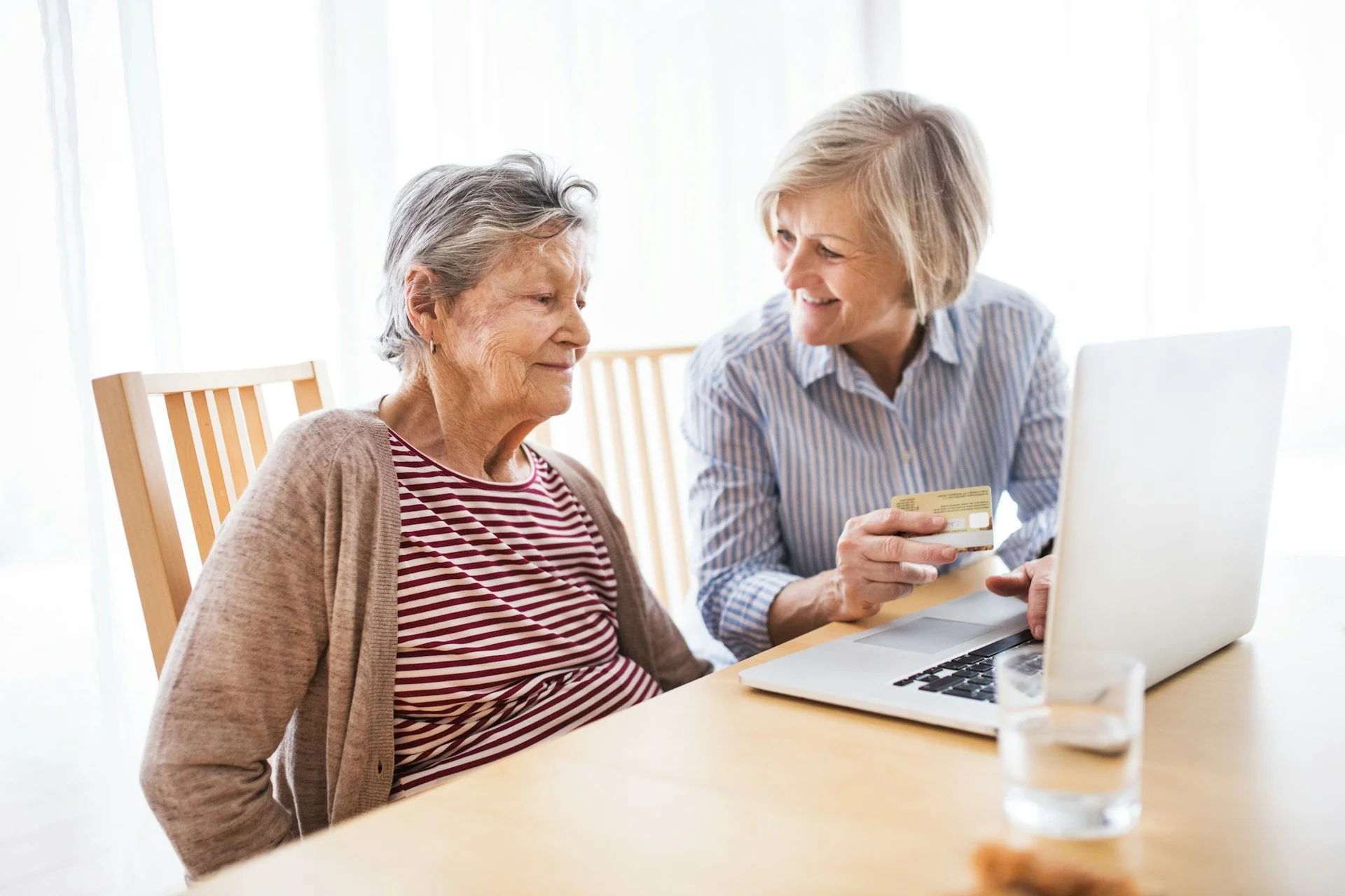 Caregiver assisting a senior woman with a laptop at home, reflecting personalized and attentive in-home support.