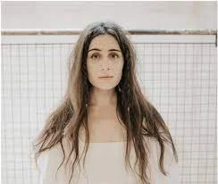 Young woman with long hair looking at the camera, standing in front of a tiled wall