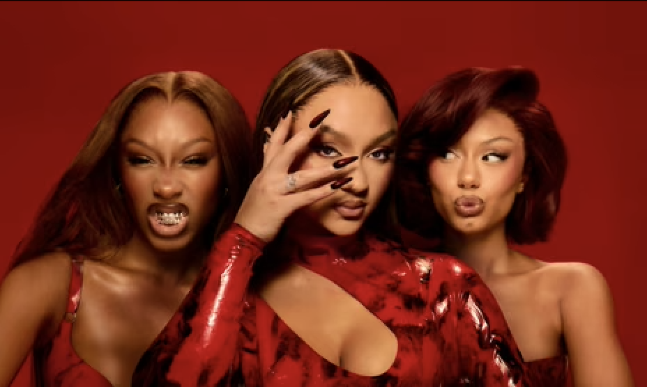 Three women wearing red outfits posing against a red background, with one woman in the middle covering one eye and making a gesture.