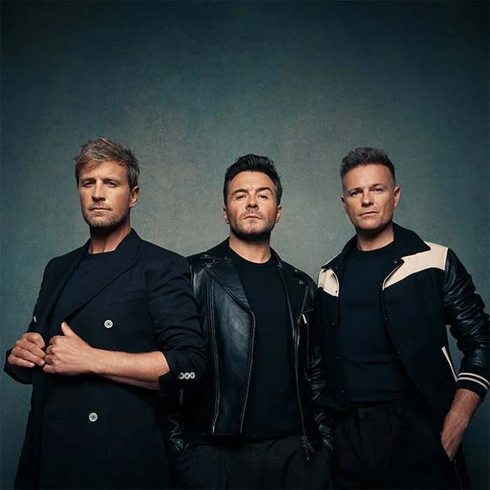 Three men posing with serious expressions against a plain background.