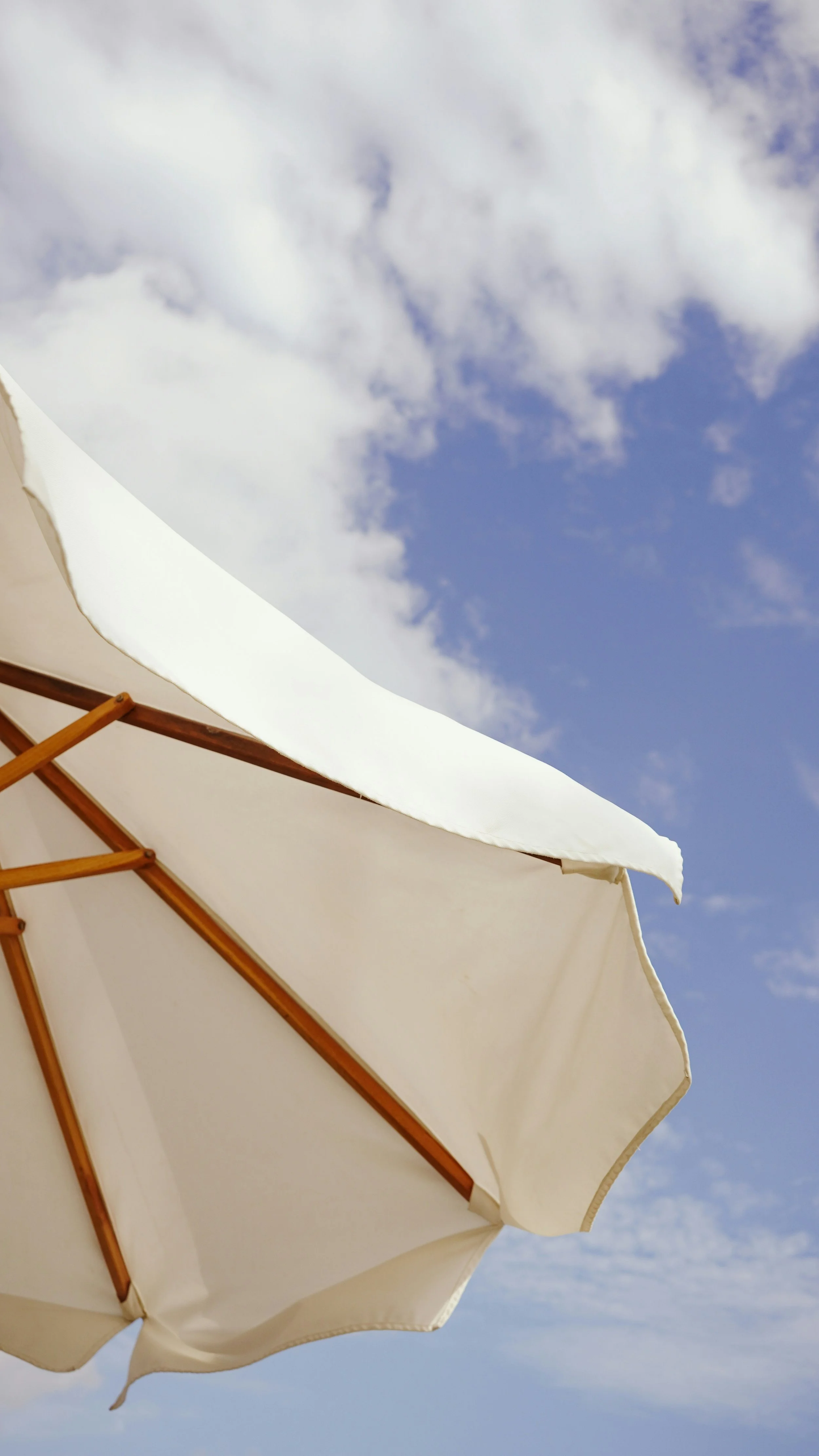 Close-up of a white beach umbrella against a blue sky with scattered clouds.