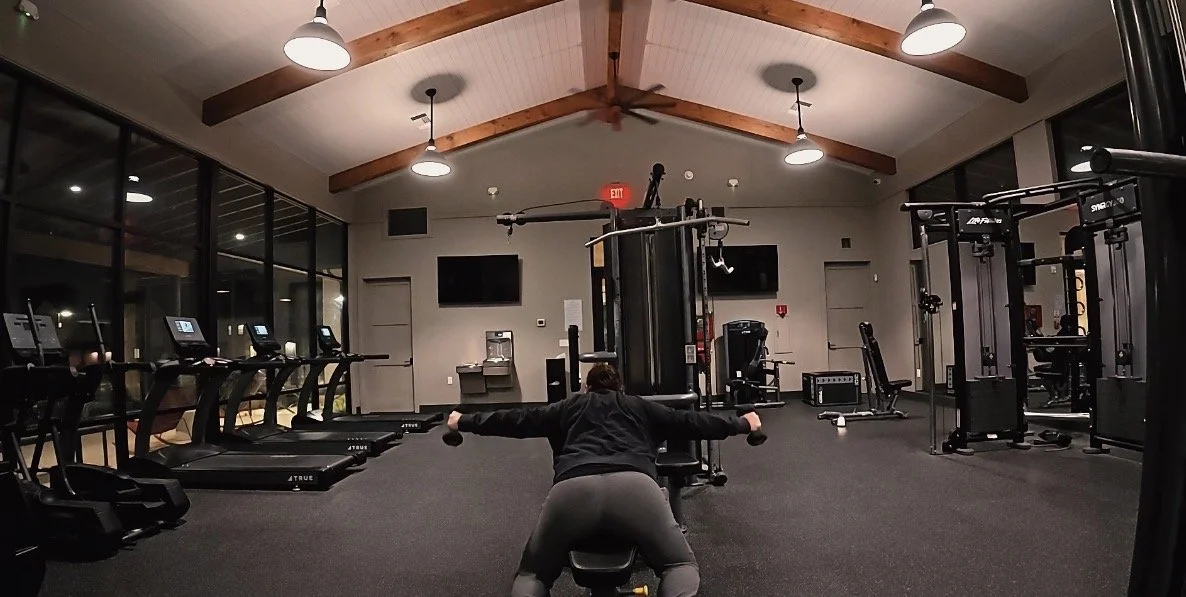 A person working out on a bench press in a gym with exercise machines and treadmills.