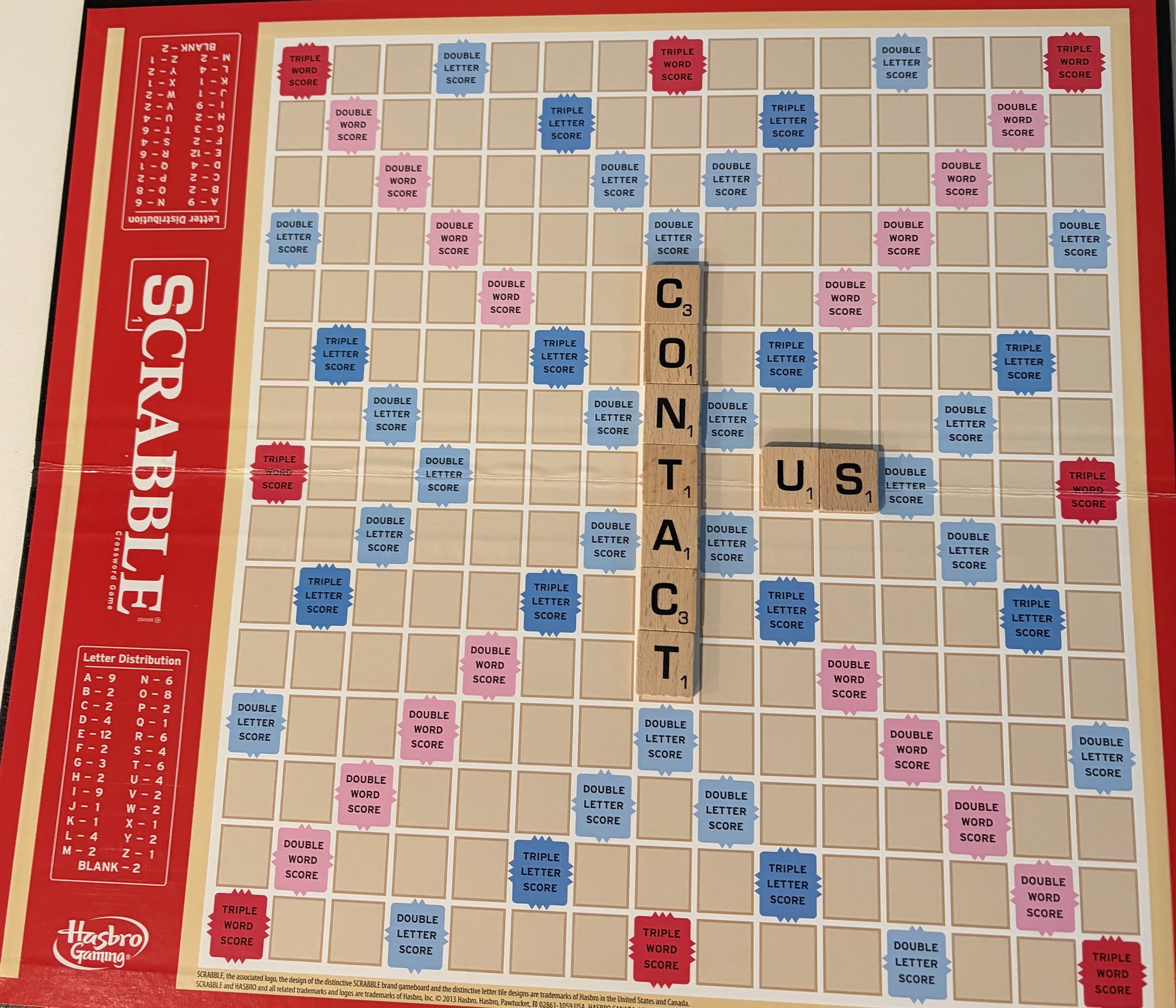Scrabble game board with premium and regular letter scores, showing the words 'CONTA(C)T' and 'US' spelled out on the grid.