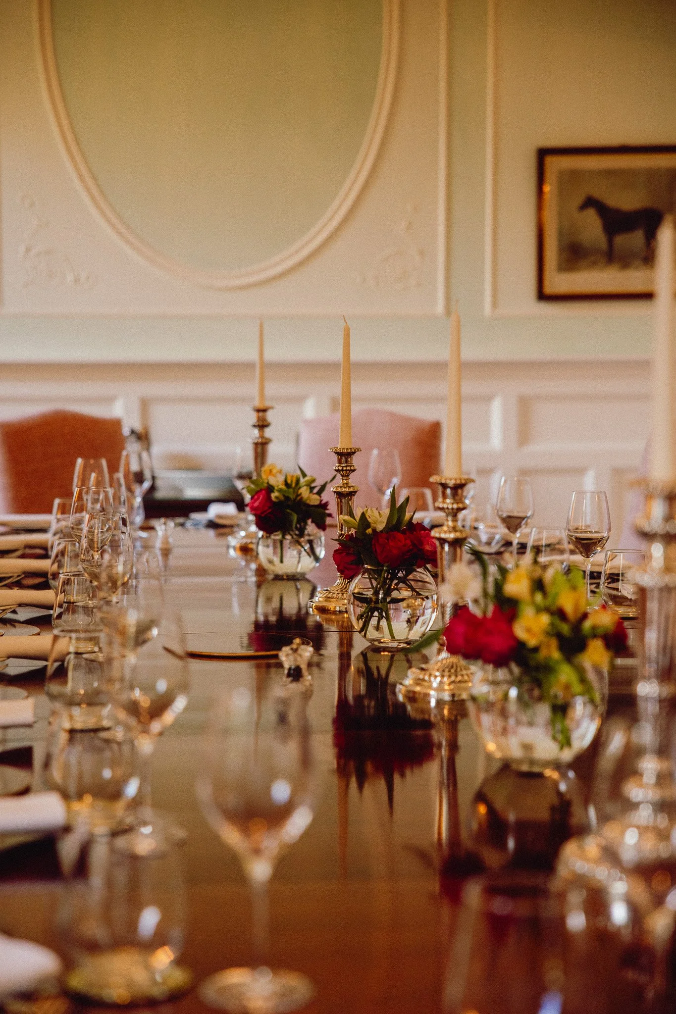 Elegant dining table set with candles, floral arrangements, wine glasses, and dinnerware in a decorated room.
