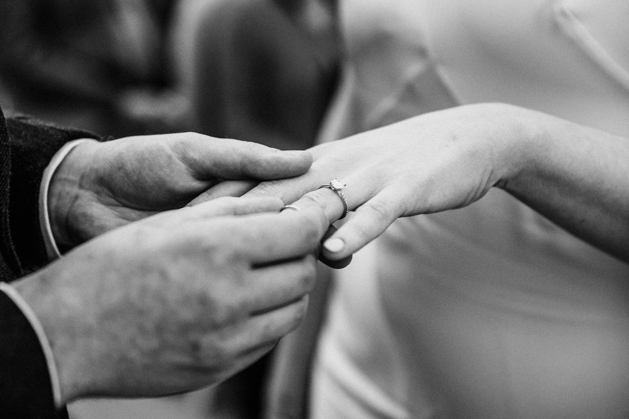 A close-up black and white photo of a person placing a ring on another person's finger during a wedding ceremony.