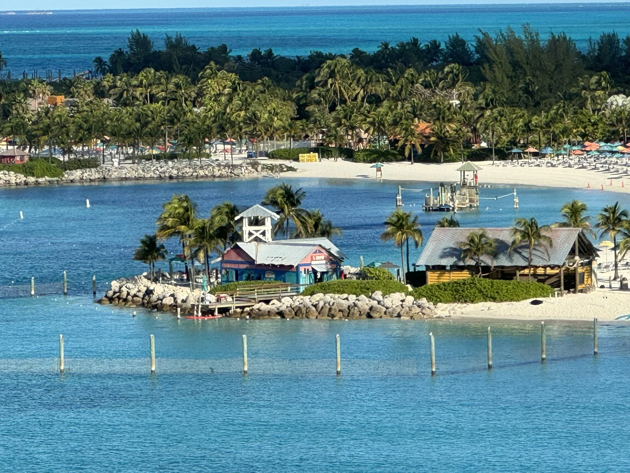 Een tropisch strand met palmbomen, een rustige waterkant en enkele kleine boten, op de achtergrond een bos en de oceaan.