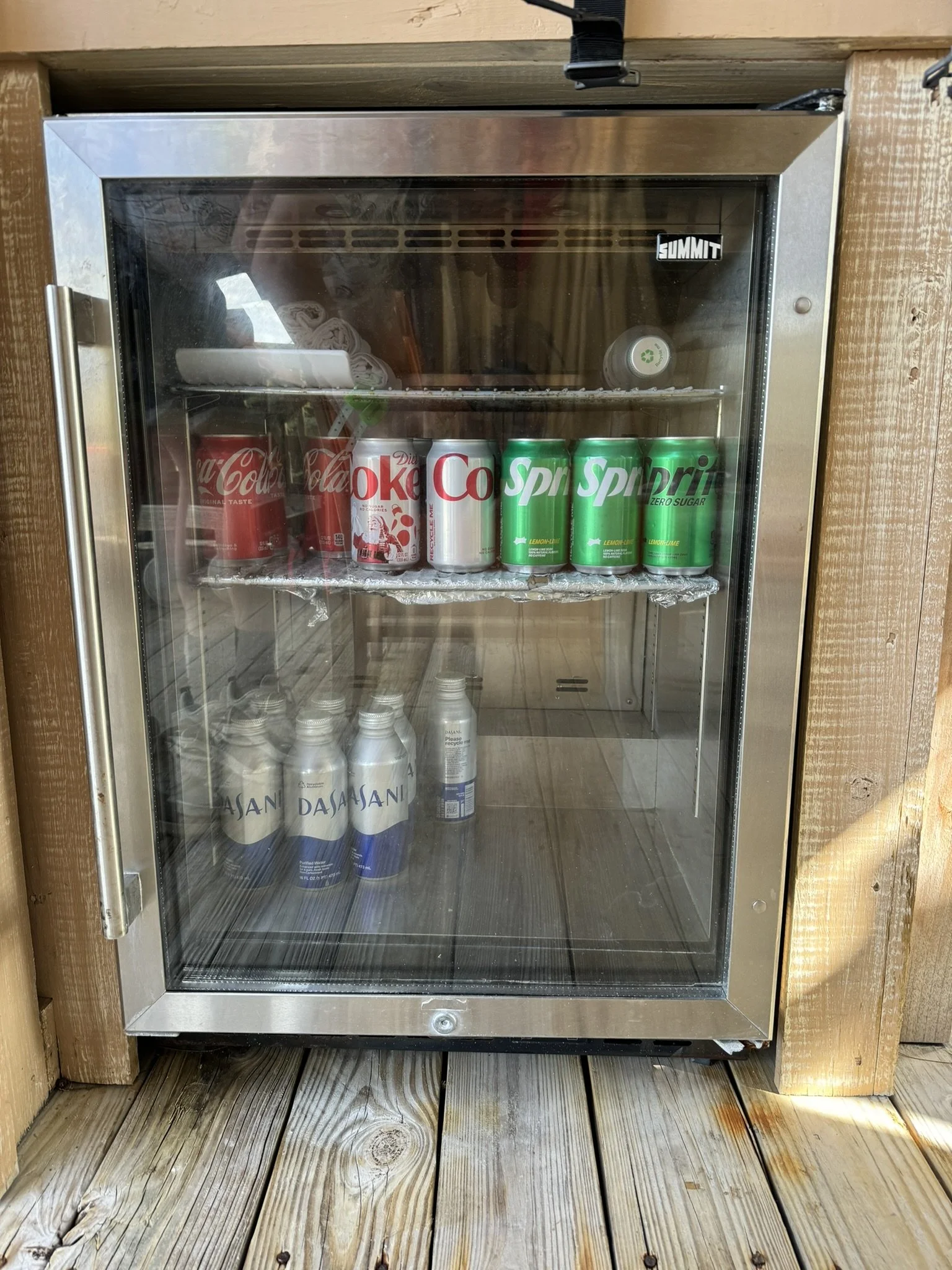 Een kleine koelkast met merken frisdrank, water en een blikje.