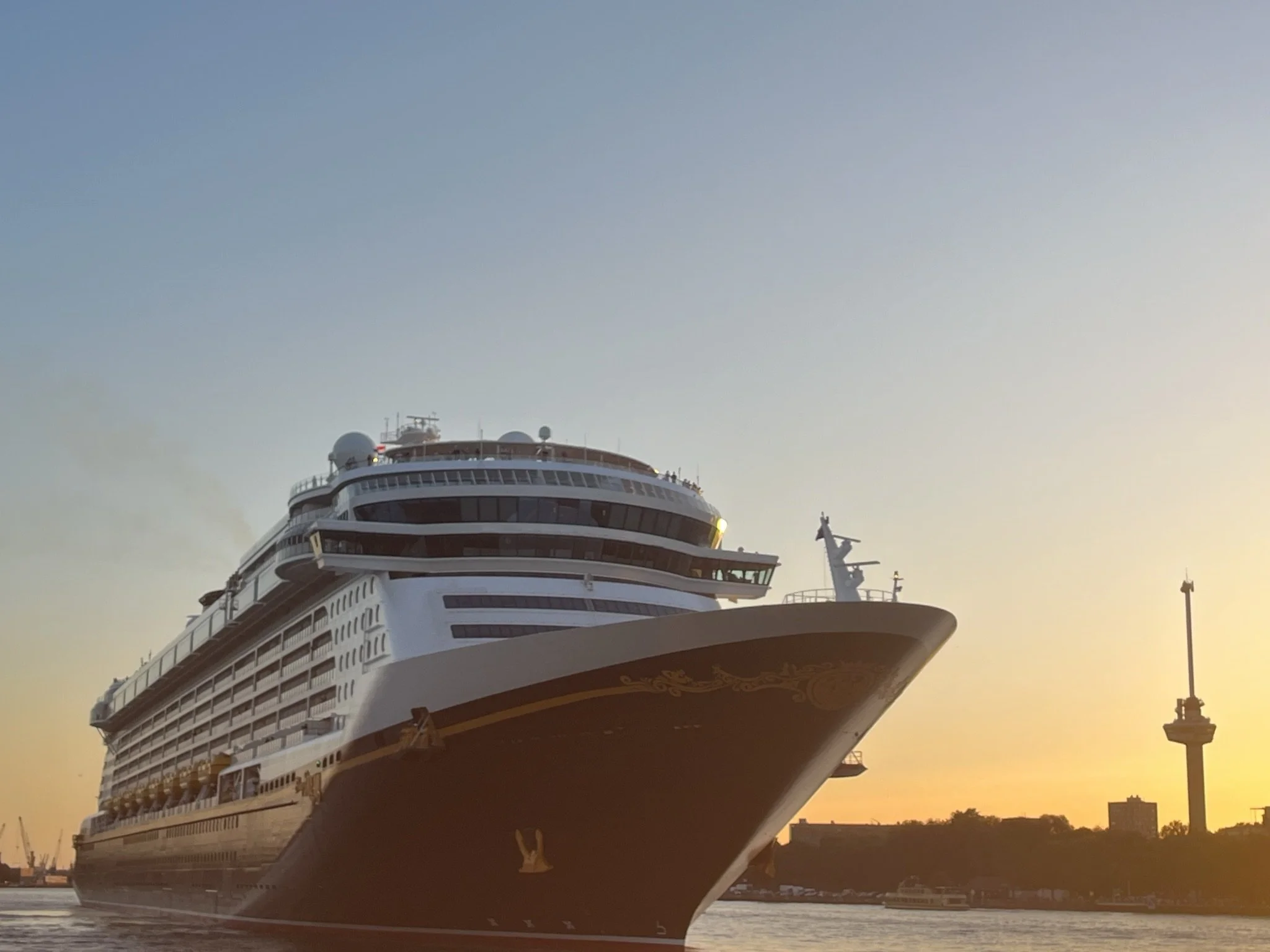 Een grote cruiseschip ligt in de haven tijdens zonsondergang, met de stad op de achtergrond.
