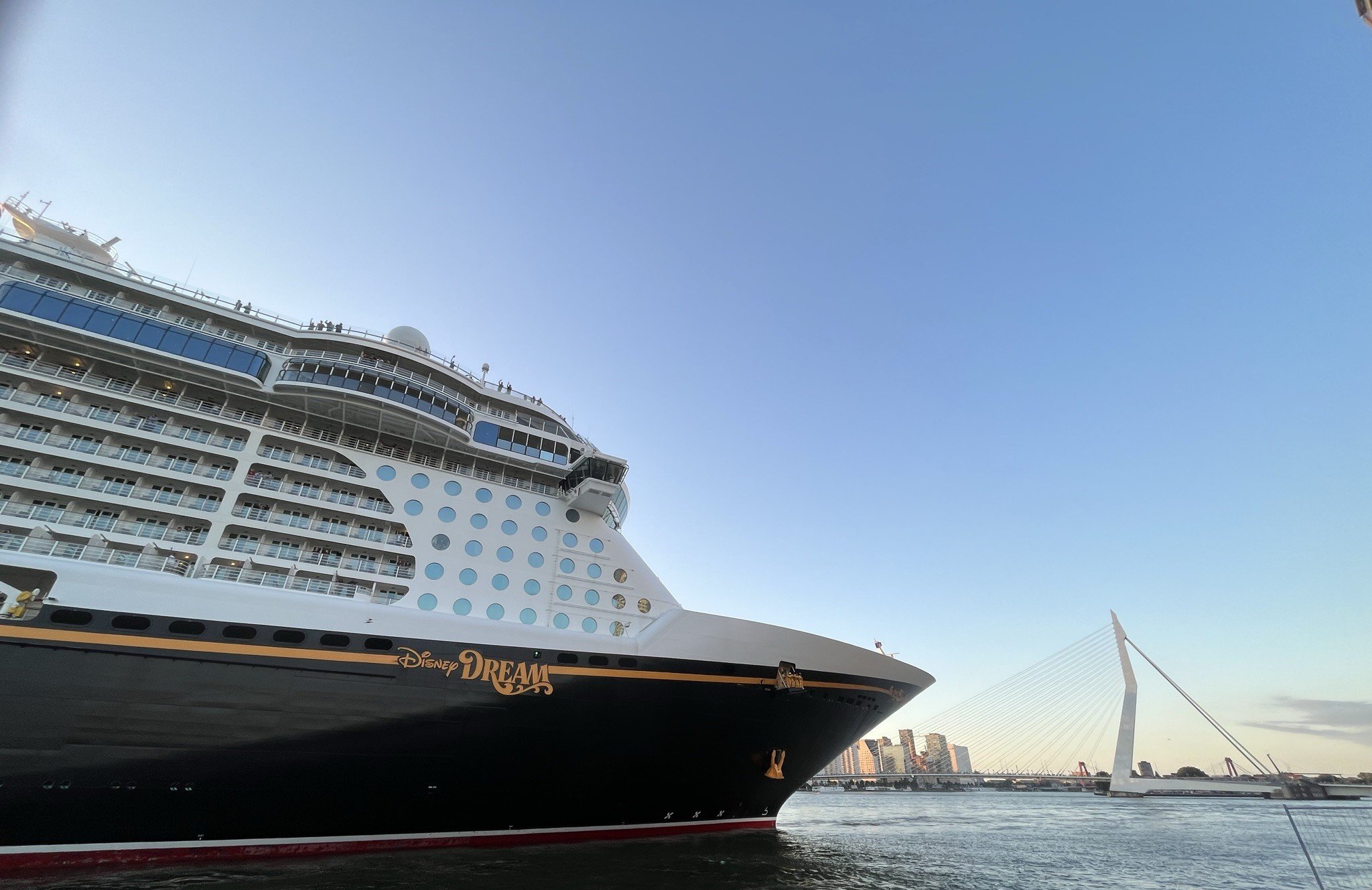Een grote Disney Dream cruiseboot ligt aangemeerd met een blauwe hemel en een brug op de achtergrond.