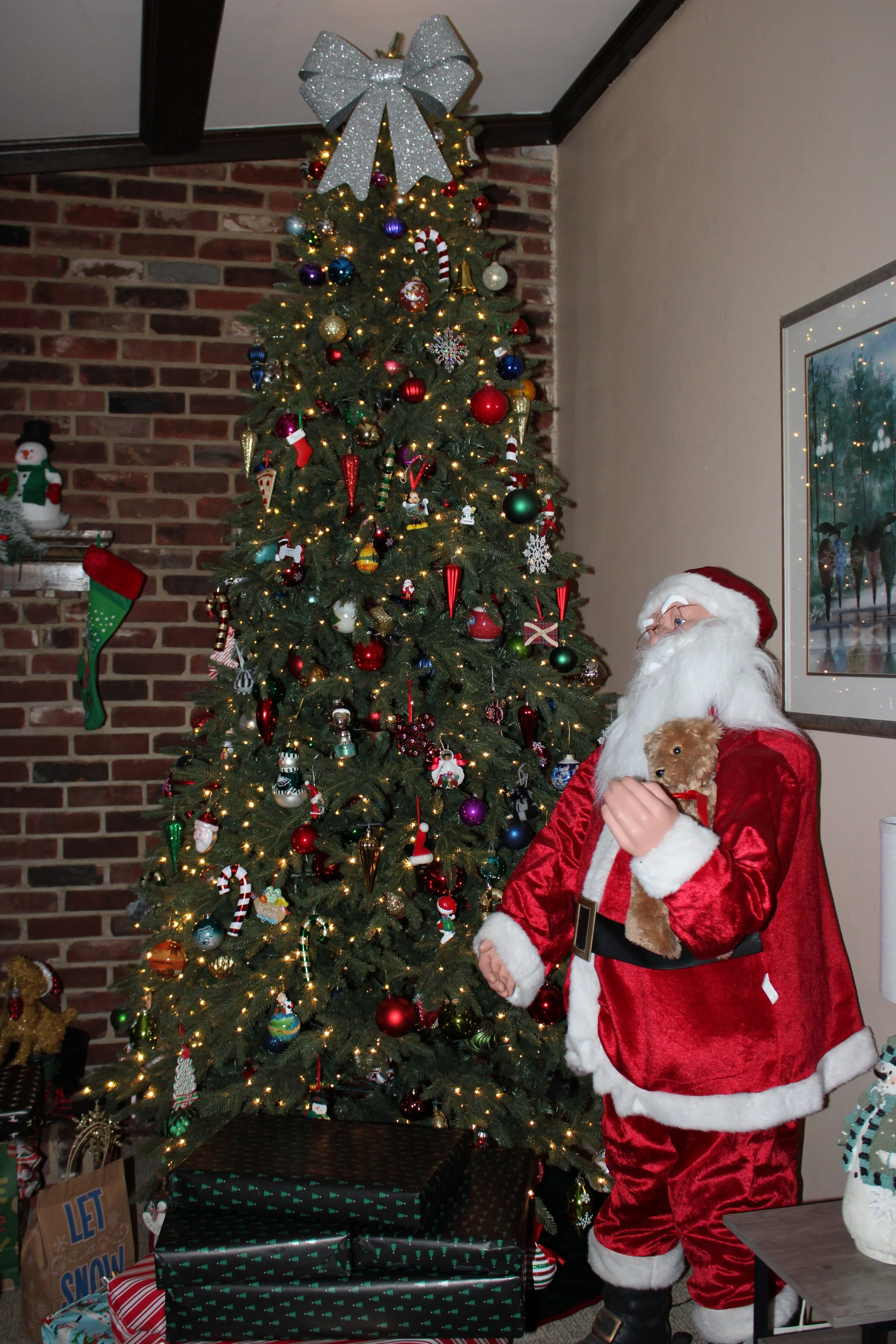 Santa Claus holding a small brown dog in front of a decorated Christmas tree with presents underneath.