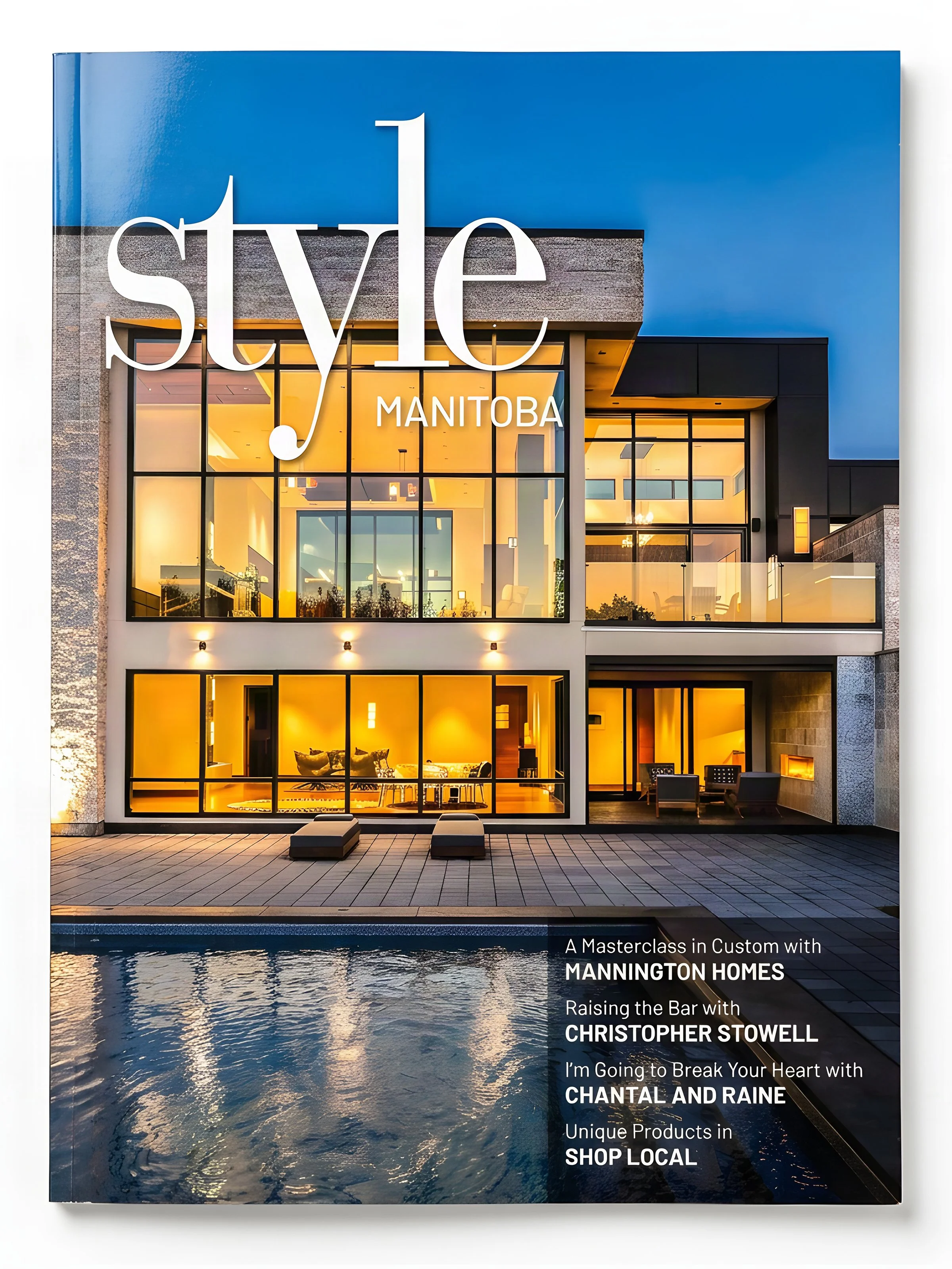 The cover of a magazine showcasing a modern building with large glass windows illuminated with warm light, situated in front of an outdoor pool. The magazine features articles on custom homes and shopping at local businesses.