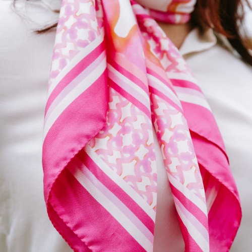 Close-up of a woman wearing a white top and a pink patterned silk scarf around her neck.