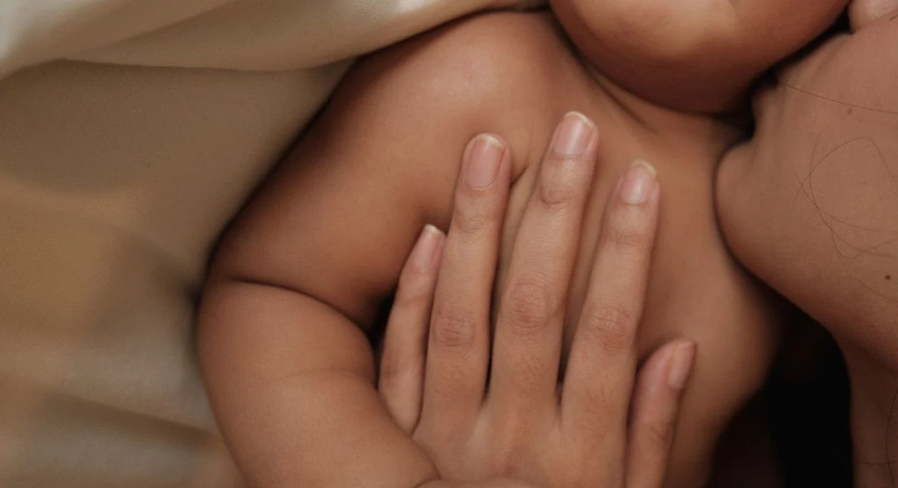 Nahaufnahme von zwei Menschen, die sich umarmen oder küssen, mit Fokus auf den oberen Rücken und den Hals einer Person. Eine Mama küsst ihr Neugeborenes. Es zeigt das Wochenbett.