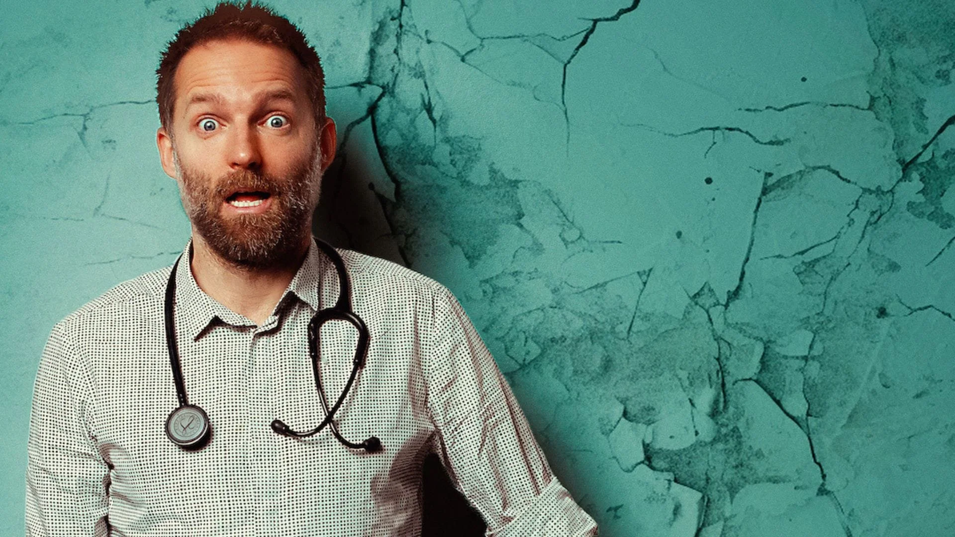Comedian Benji Waterhouse with reddish hair and a beard, wearing a black and white checkered shirt with a stethoscope around his neck, looks surprised against a teal, cracked wall background.