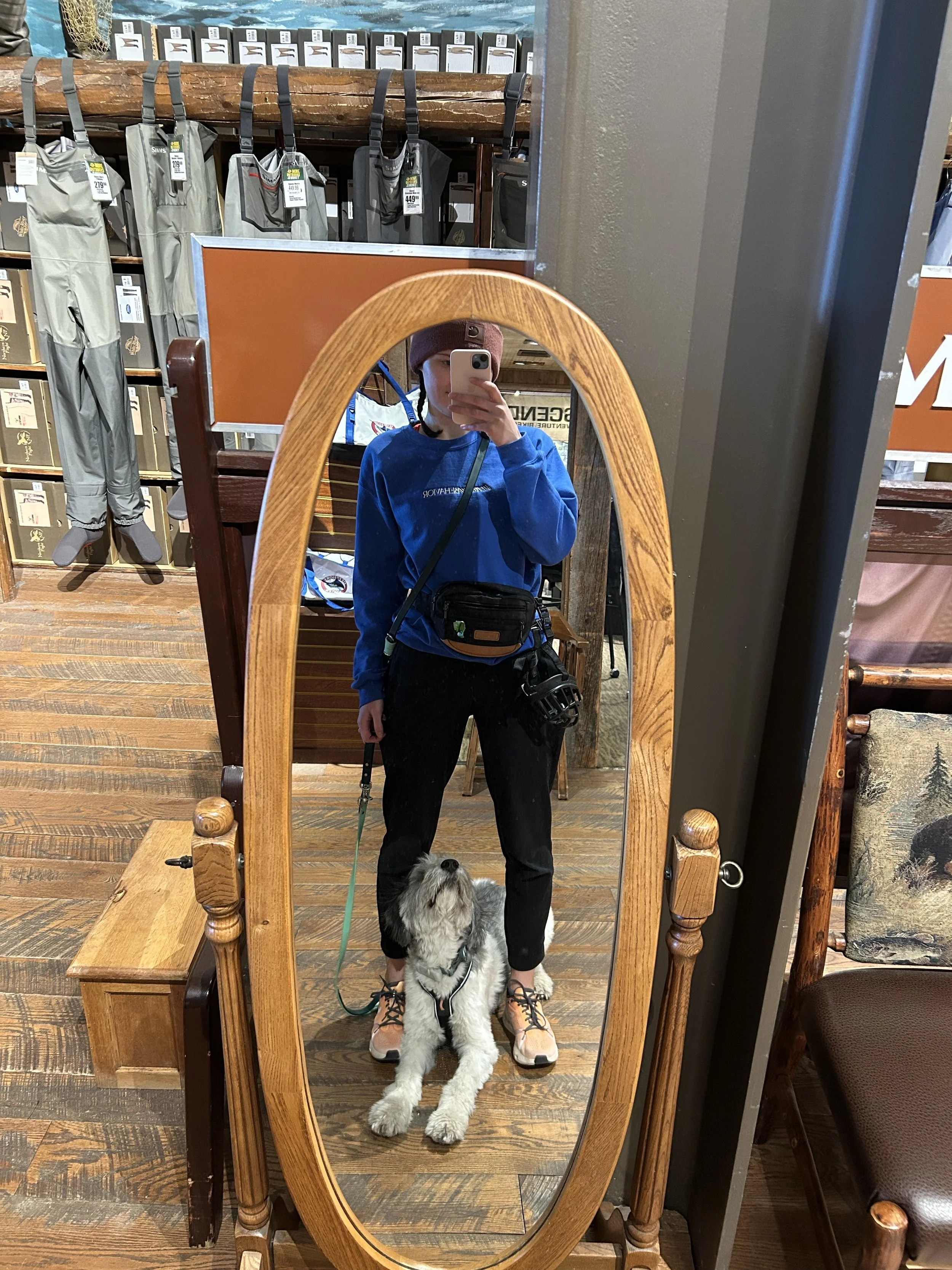 A woman standing in front of a mirror with her dog looking up at her