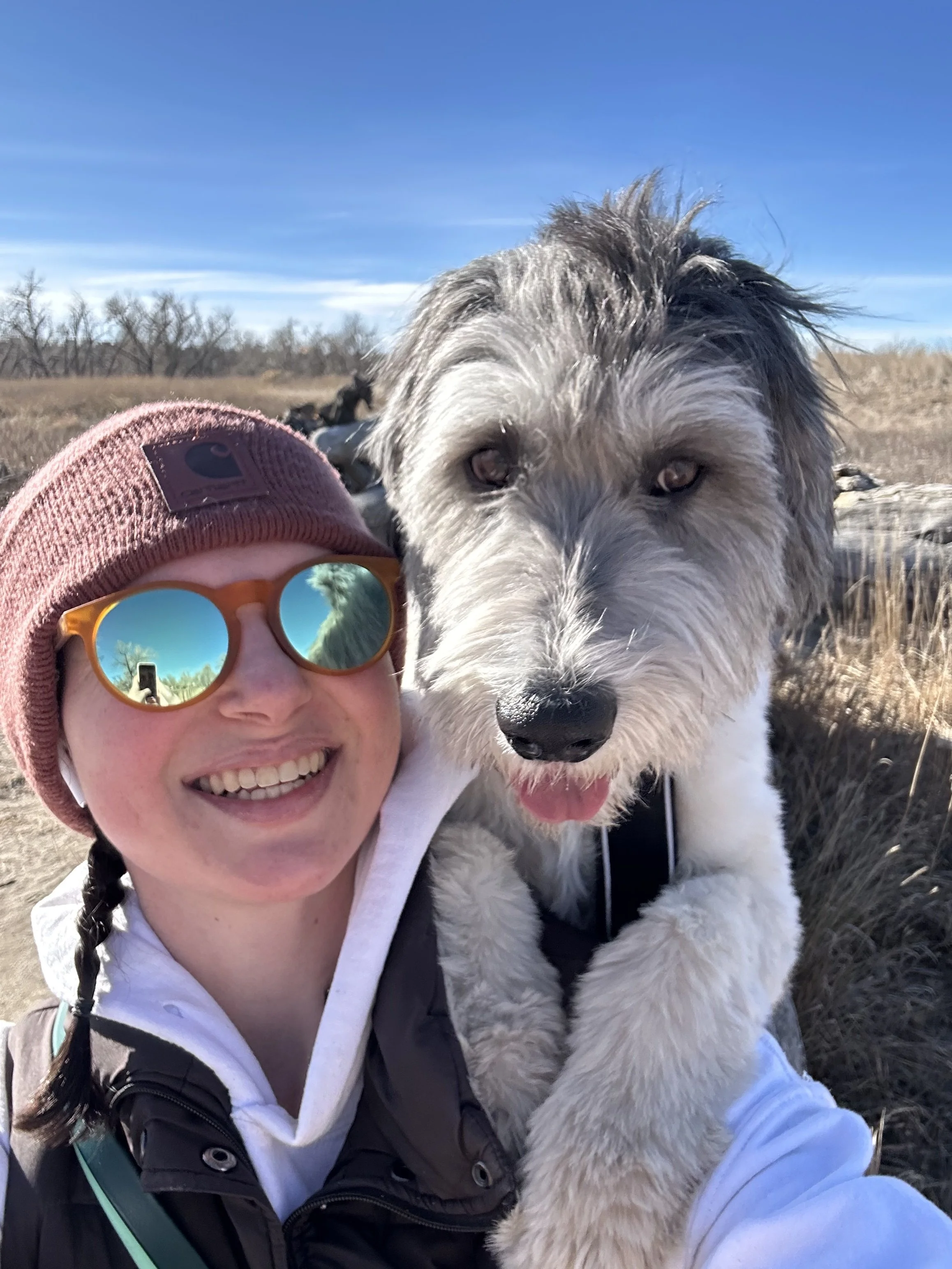 A woman taking a selfie with her dog peeking over her shoulder