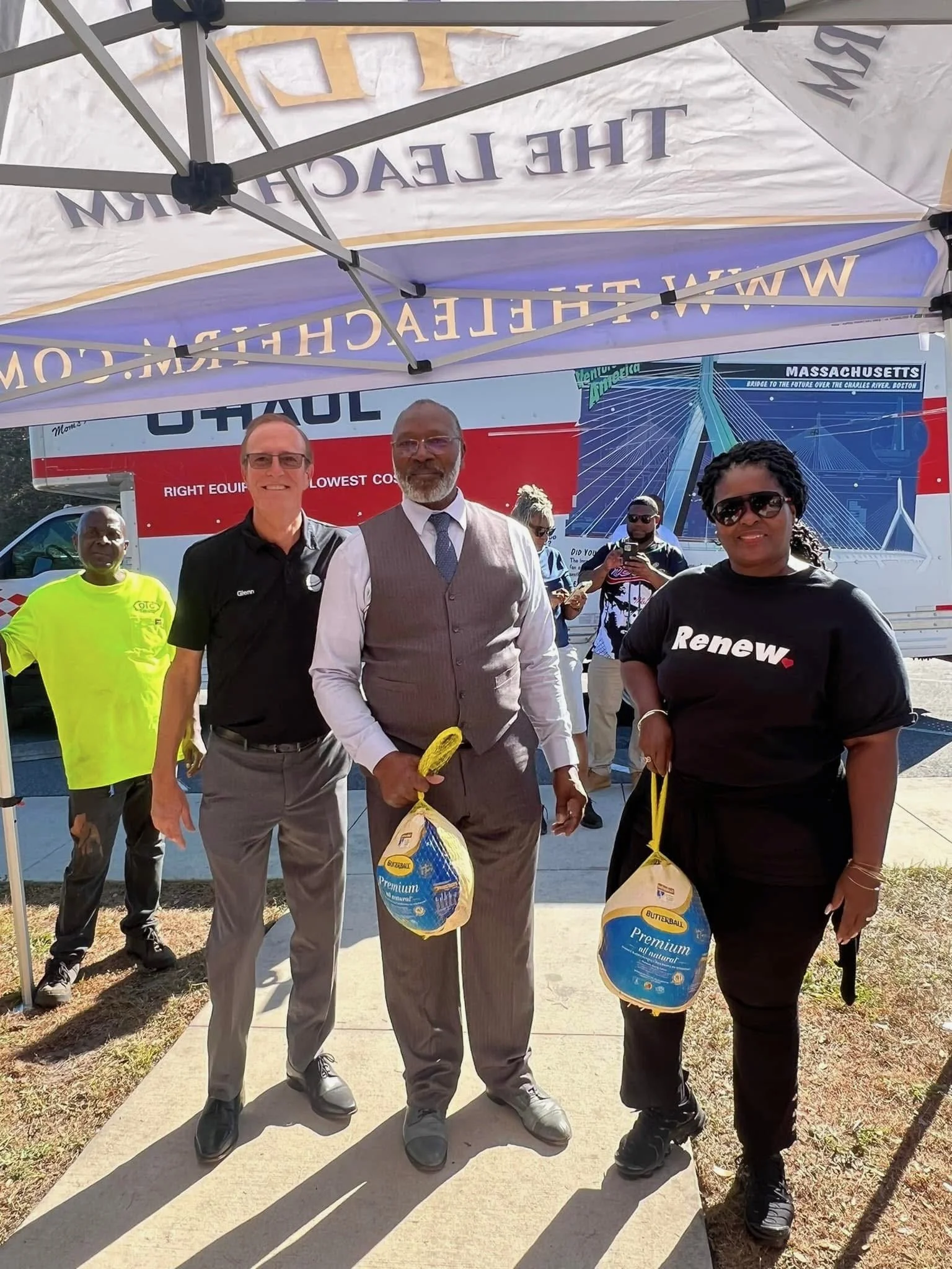Three people standing outdoors under a tent, holding bags of butter.