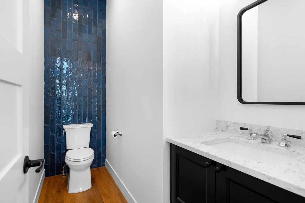 Bathroom with white toilet and black vanity with a marble countertop, single sink, and a rectangular mirror.