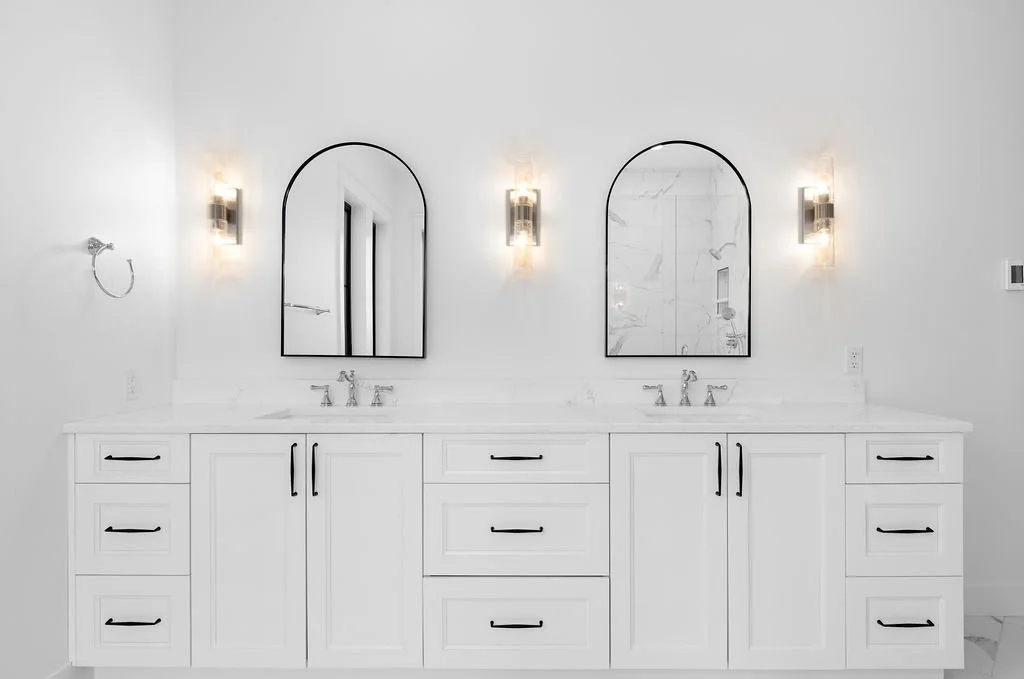 Double vanity bathroom with white cabinets, marble countertops, and two oval mirrors, flanked by wall-mounted lights.