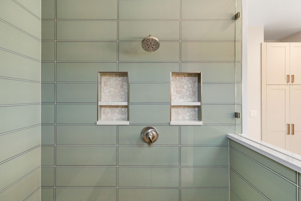 A modern shower with green tiled walls, two built-in niches with mosaic tile backgrounds, a ceiling-mounted showerhead, and a silver shower control handle.