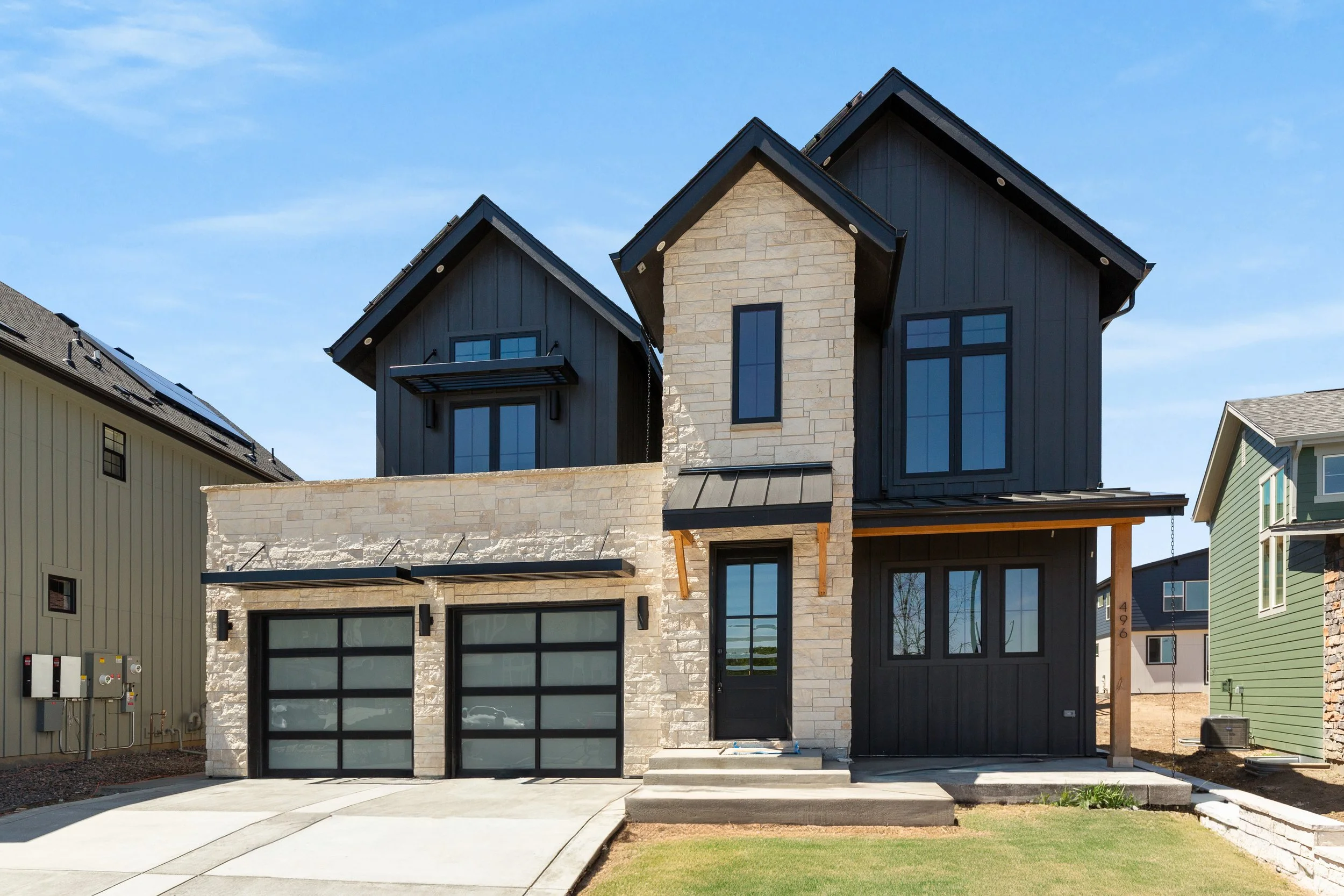 Front view of a modern two-story house with black and stone exterior, large windows, two garage doors, and a small front porch with steps.