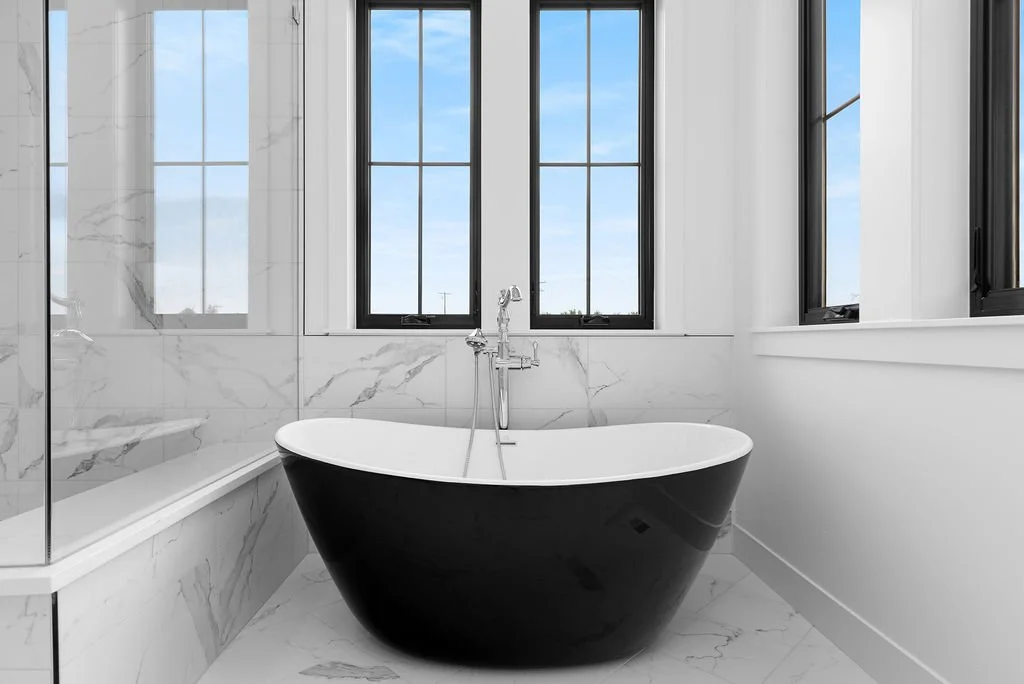 Modern bathroom with a black freestanding bathtub and large windows showing a cloudy sky
