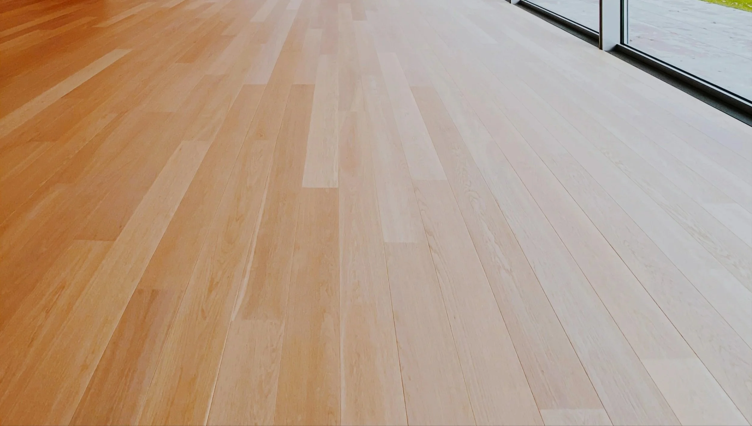 Light-colored wooden flooring near a glass window with a view outside.