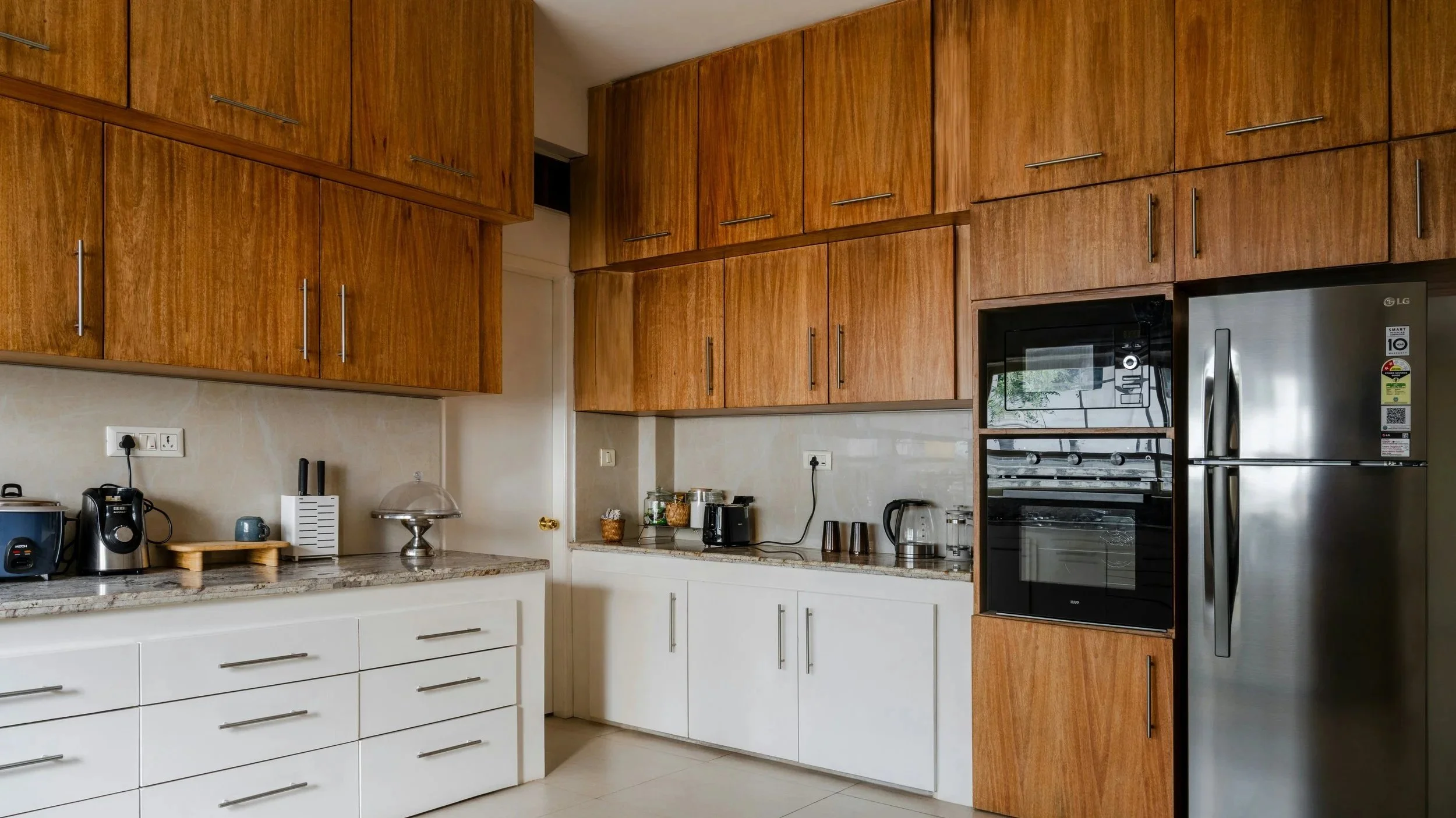 Modern kitchen with wooden cabinets, white drawers, granite countertops, black and silver appliances including a refrigerator, oven, and microwave, and various small kitchen appliances on the counter.
