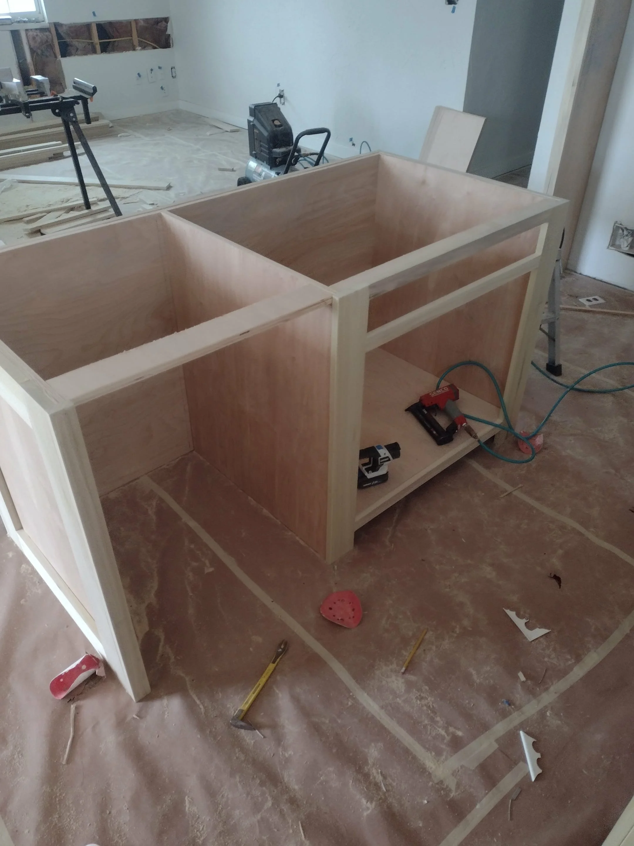 Wooden frame of a furniture piece under construction in a room with tools, measuring tape, and construction debris on the floor.