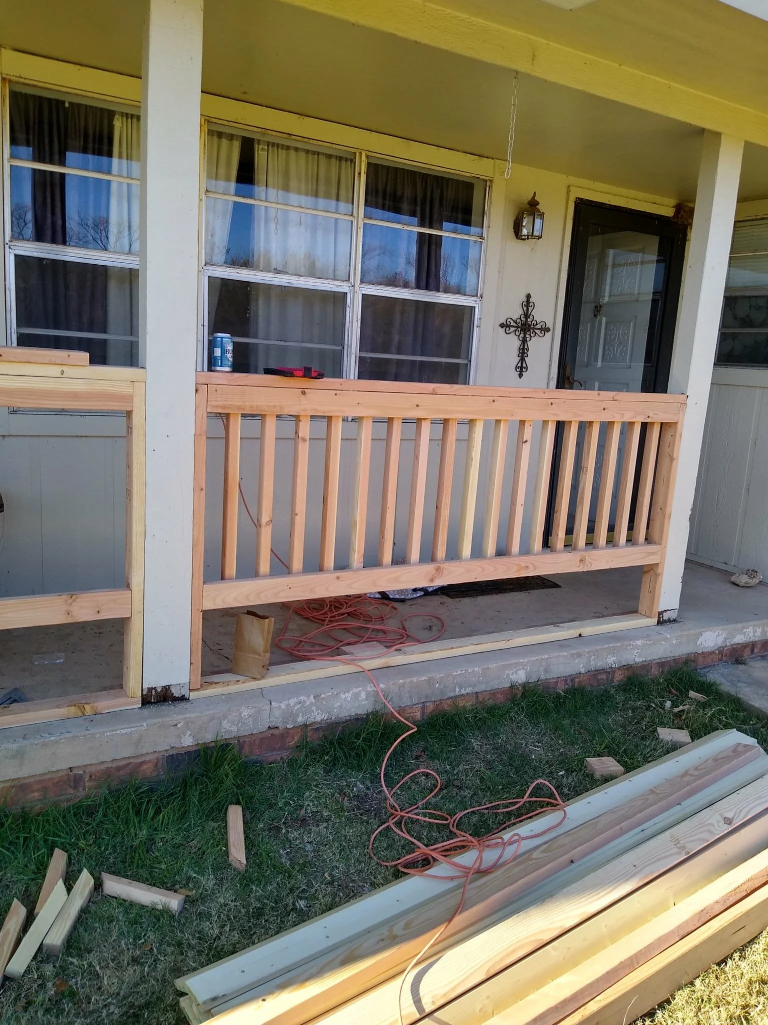 A front porch under renovation with a newly built wooden railing, construction tools, and materials scattered on the ground.
