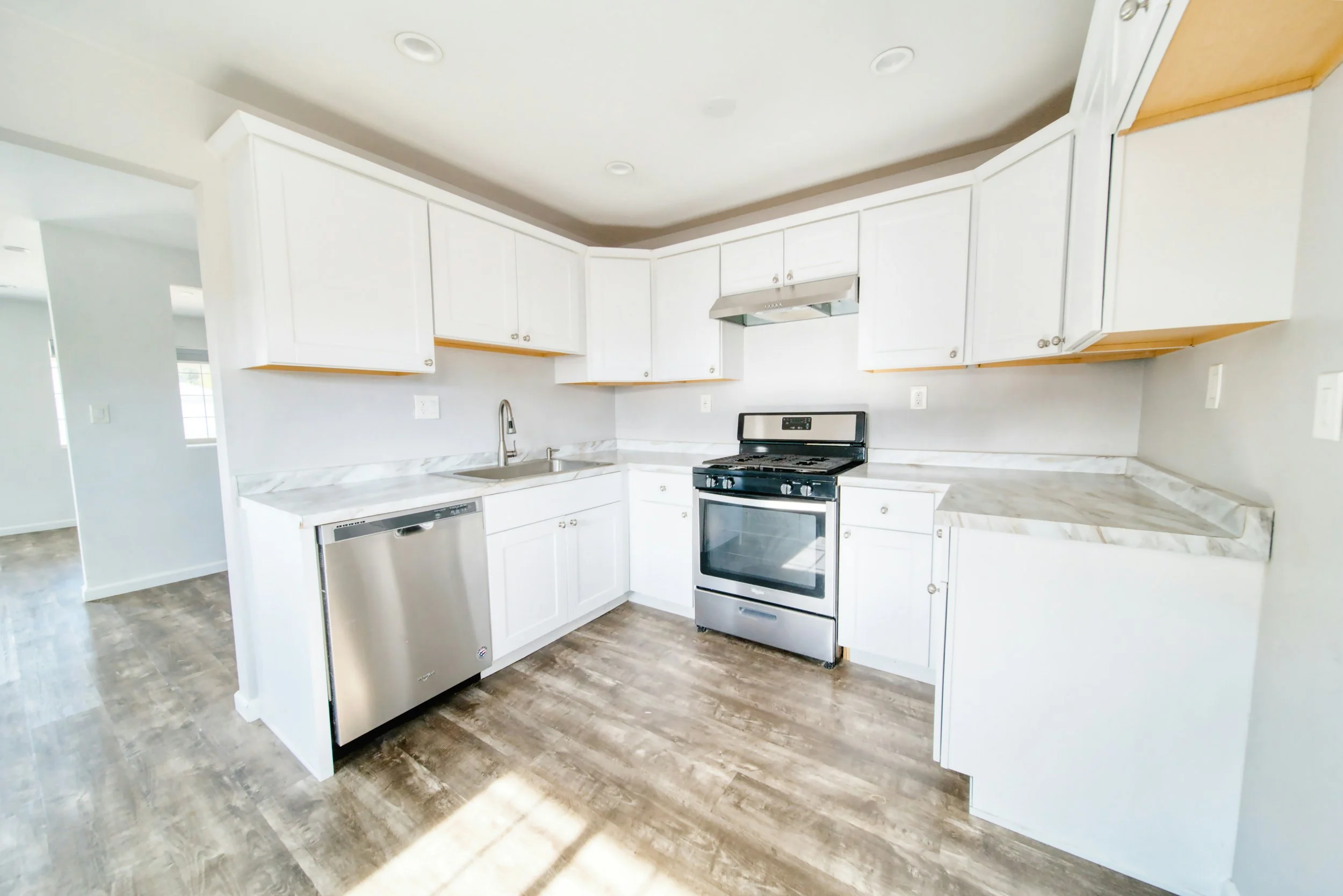 Modern kitchen with white cabinets, stainless steel dishwasher, black stove, marble countertops, and hardwood flooring.