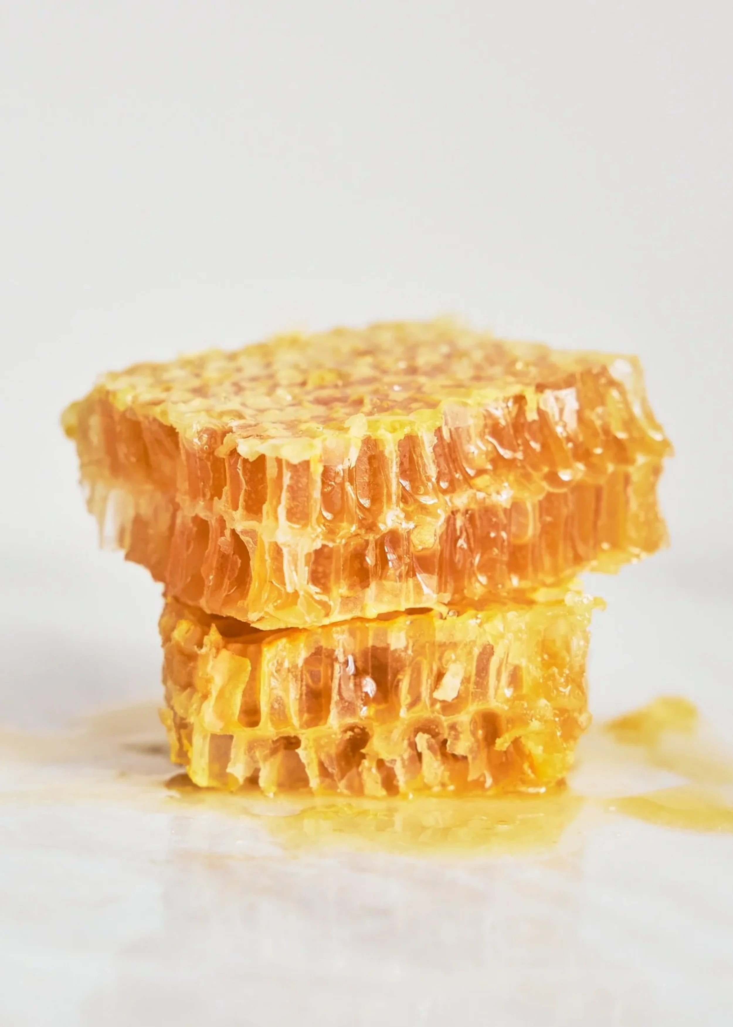 Close-up of a honeycomb with honey dripping from it, set against a white background.