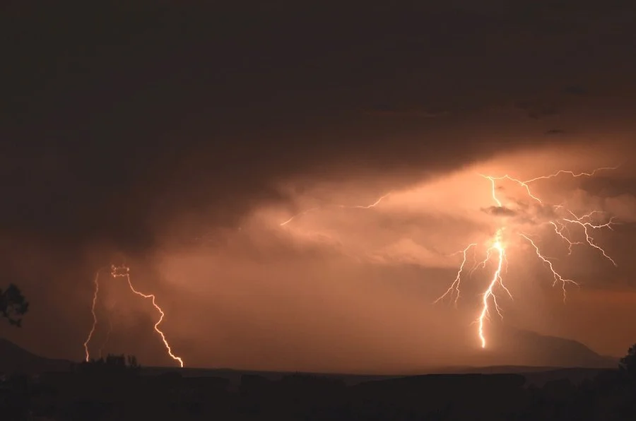 Lightning strikes during a thunderstorm over a dark landscape at night.