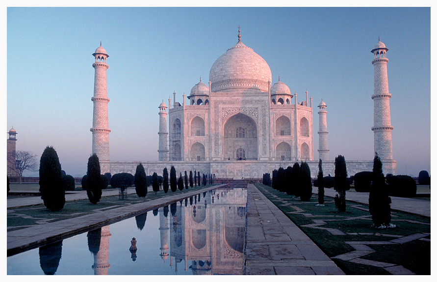 The Taj Mahal reflected in a pool with a clear blue sky in the background.