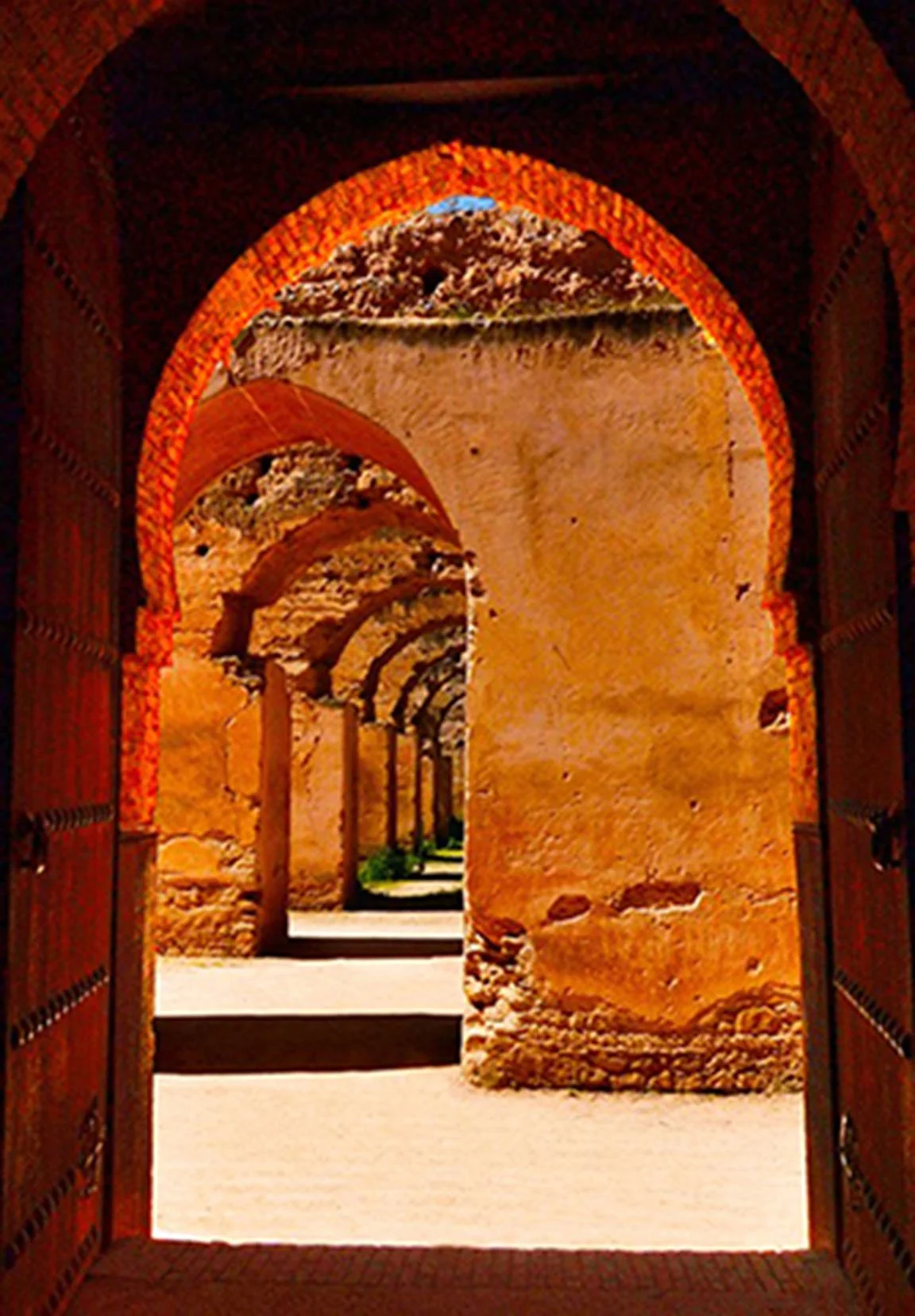 View through an arched door of a series of stone archways in a desert setting.