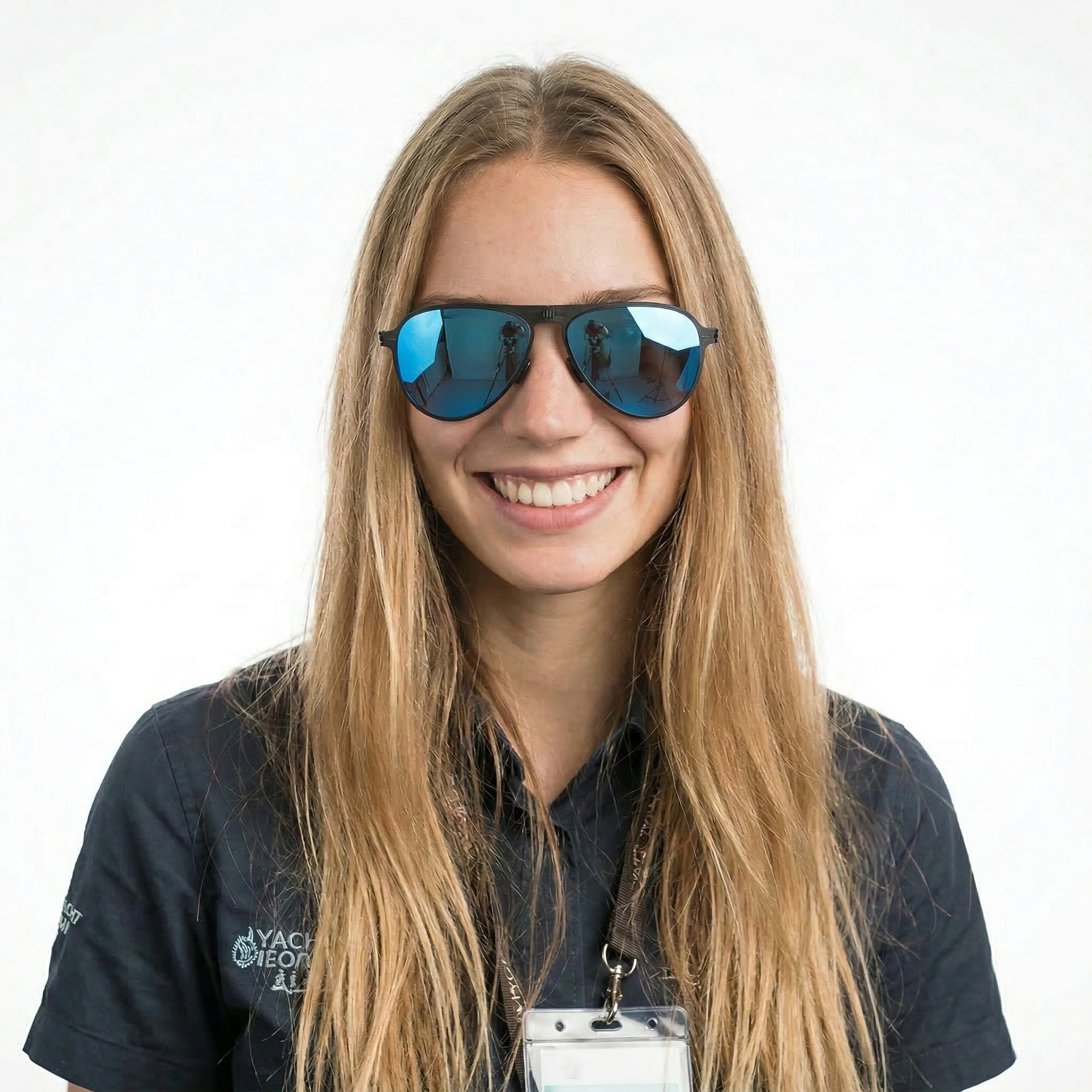 Close-up of a woman with long blonde hair wearing reflective sunglasses and a black uniform with a badge and lanyard against a white background.